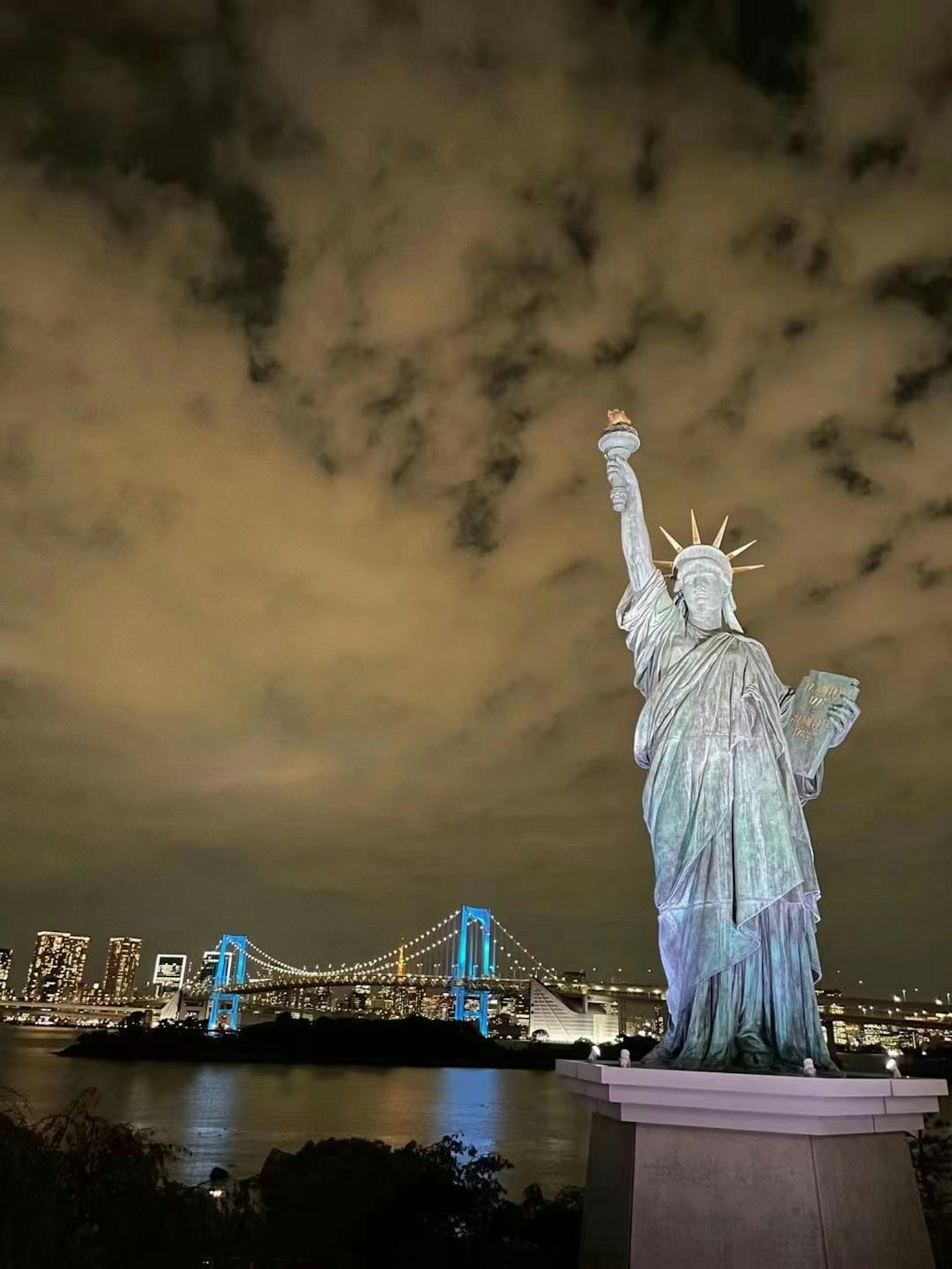 夜晚的自由女神像俯瞰东京湾和背景中的彩虹桥