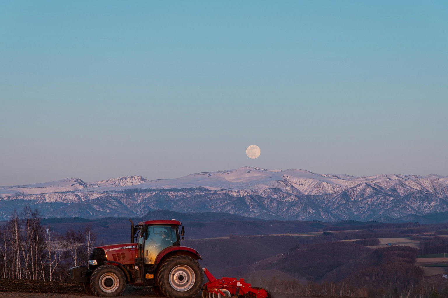 Tracteur dans un paysage avec des montagnes enneigées et une pleine lune