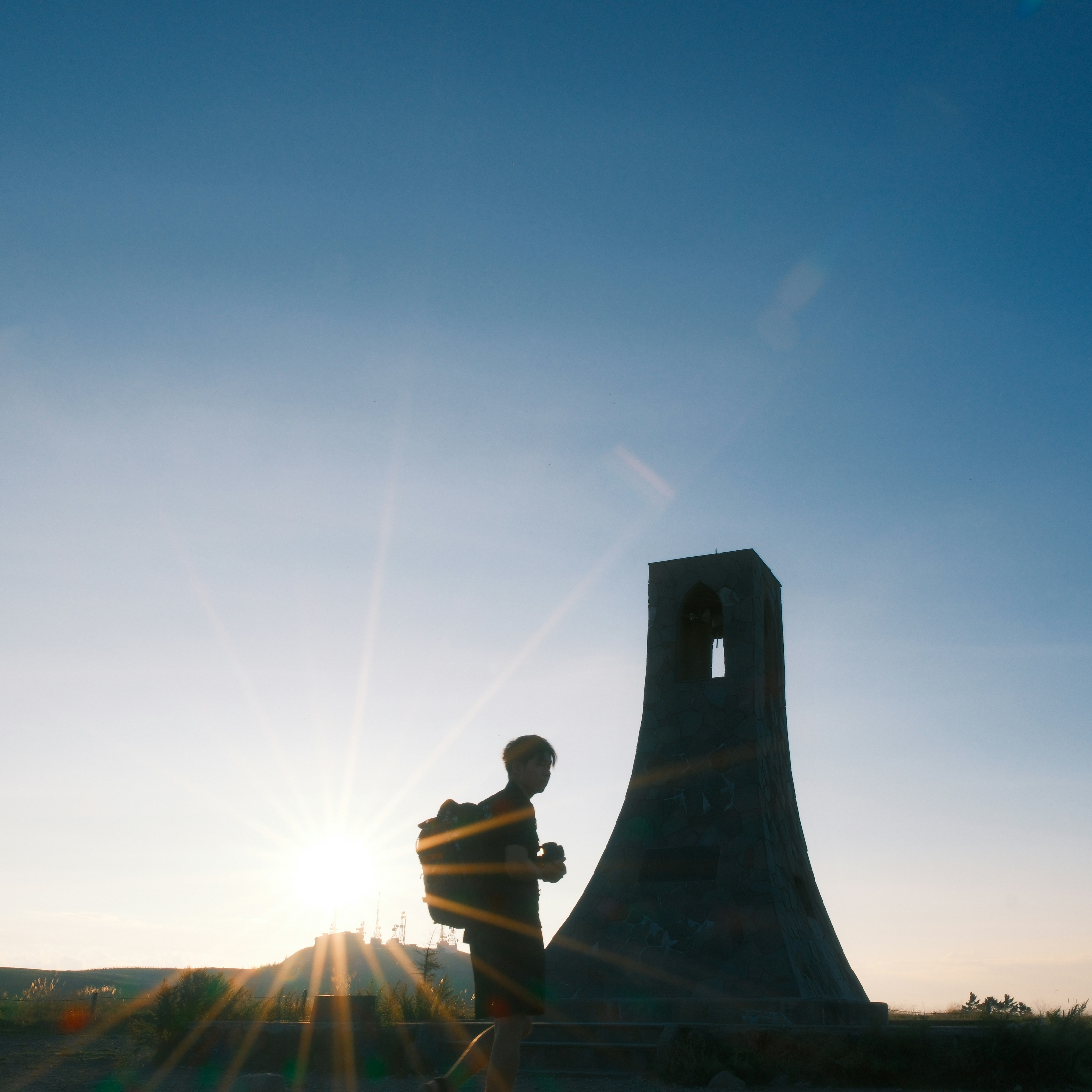 silhouette of a person standing beside a stone monument at sunset
