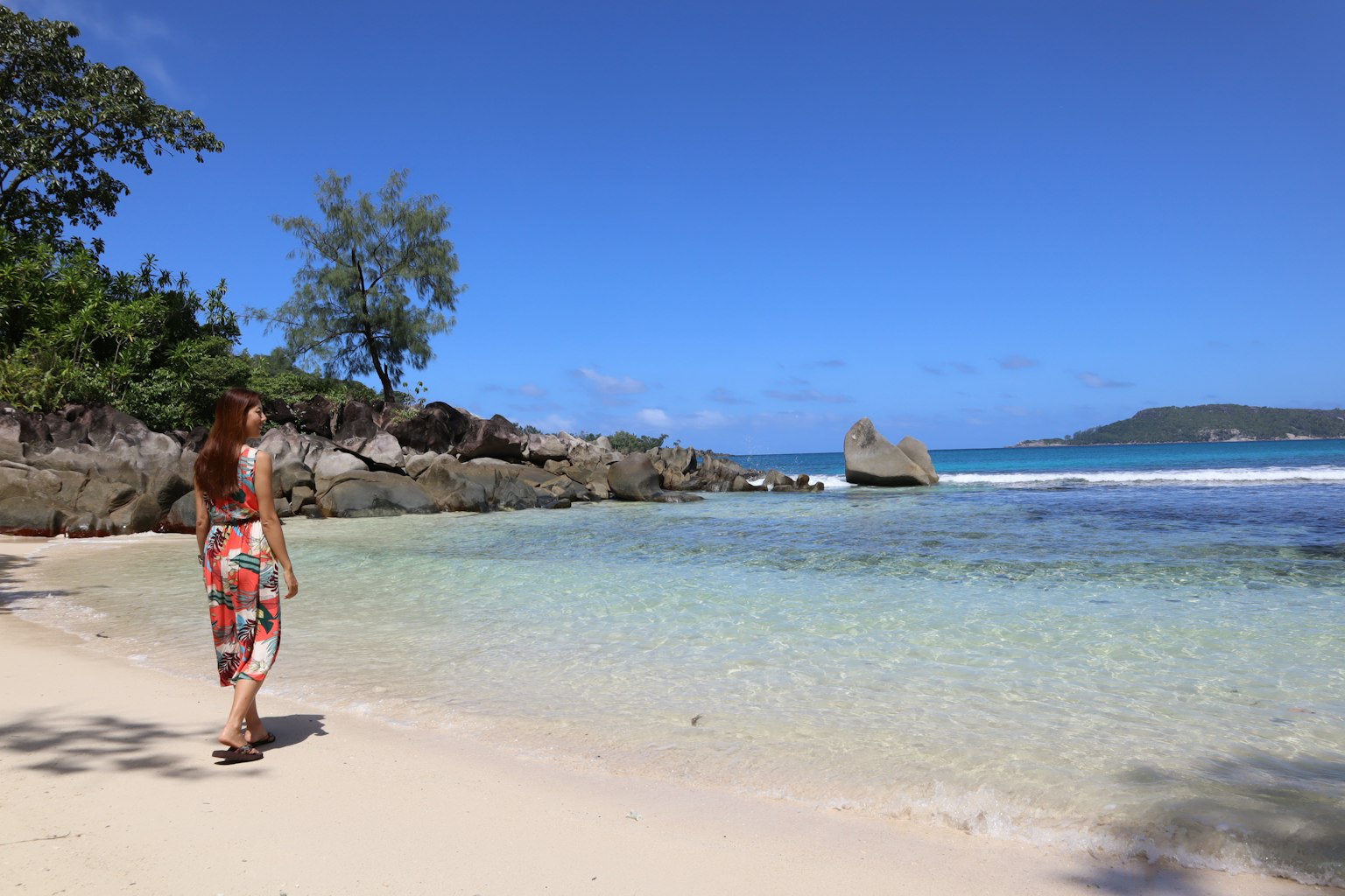 Frau, die an einem schönen Strand mit klarem blauen Himmel und ruhigem Meer spaziert