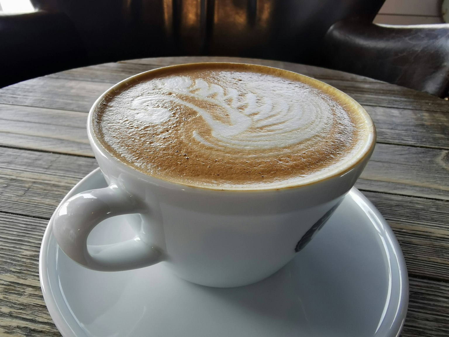 A white cup filled with latte featuring intricate latte art