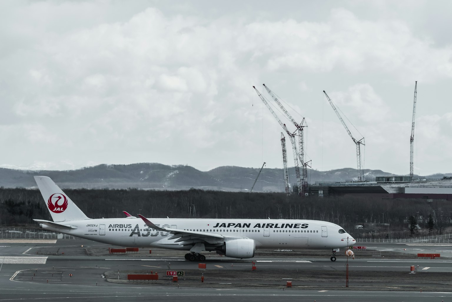 Japan Airlines airplane taxiing on runway with cranes in background