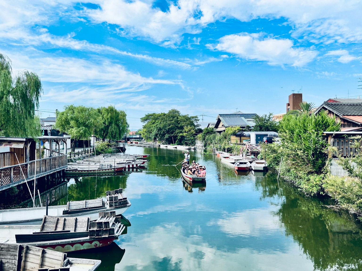 Ruhiger Kanal mit Booten, die den blauen Himmel und Wolken spiegeln, umgeben von üppigem Grün