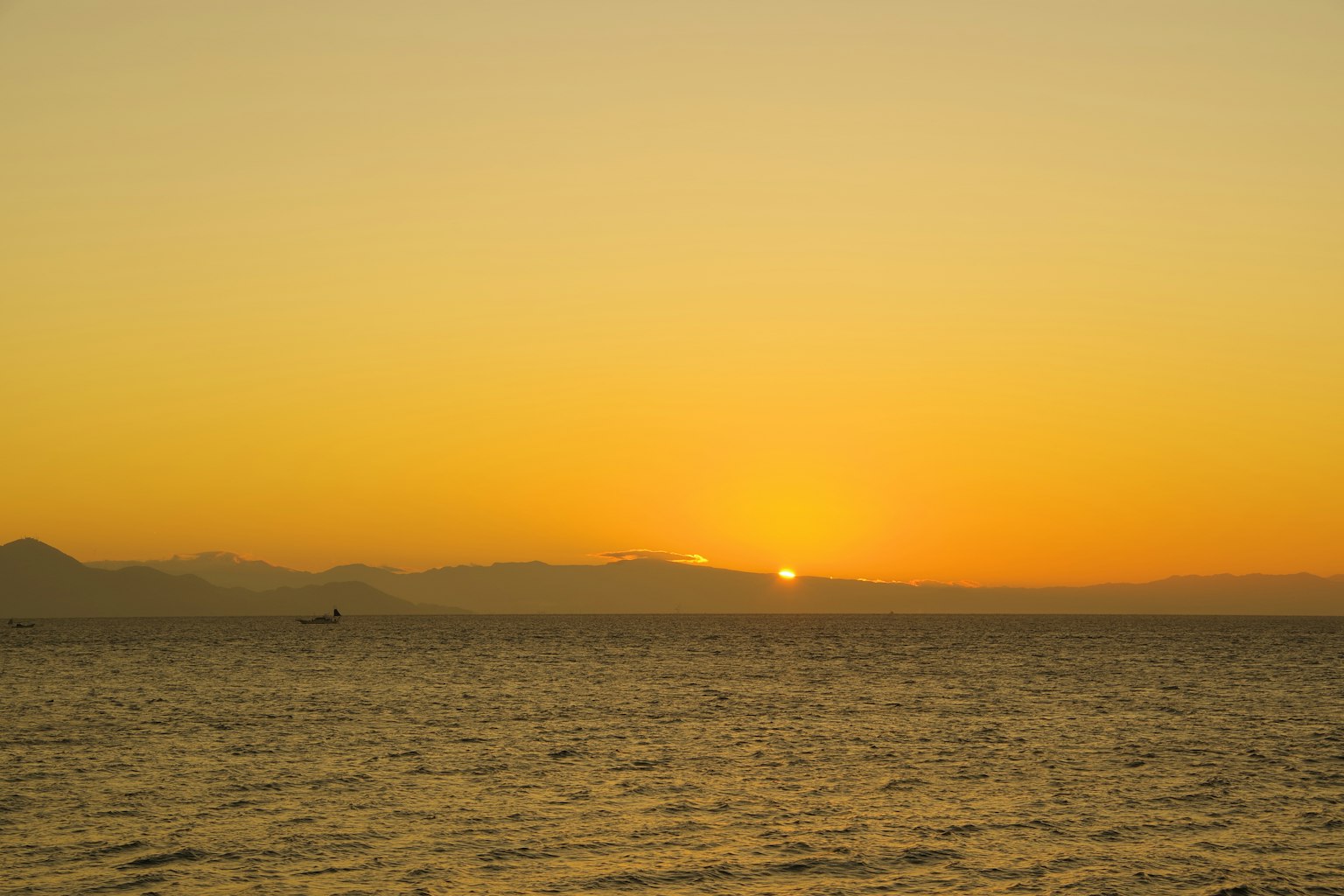 Paesaggio marino al tramonto con cielo arancione e silhouette di montagne