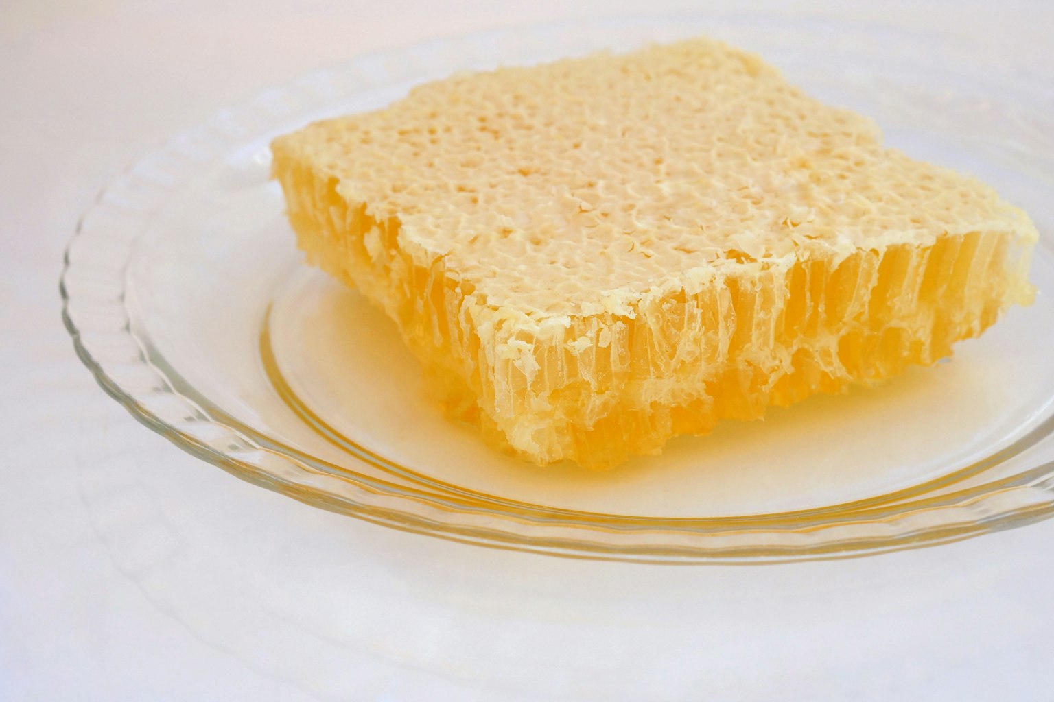 A translucent honeycomb structure of honey placed on a clear plate