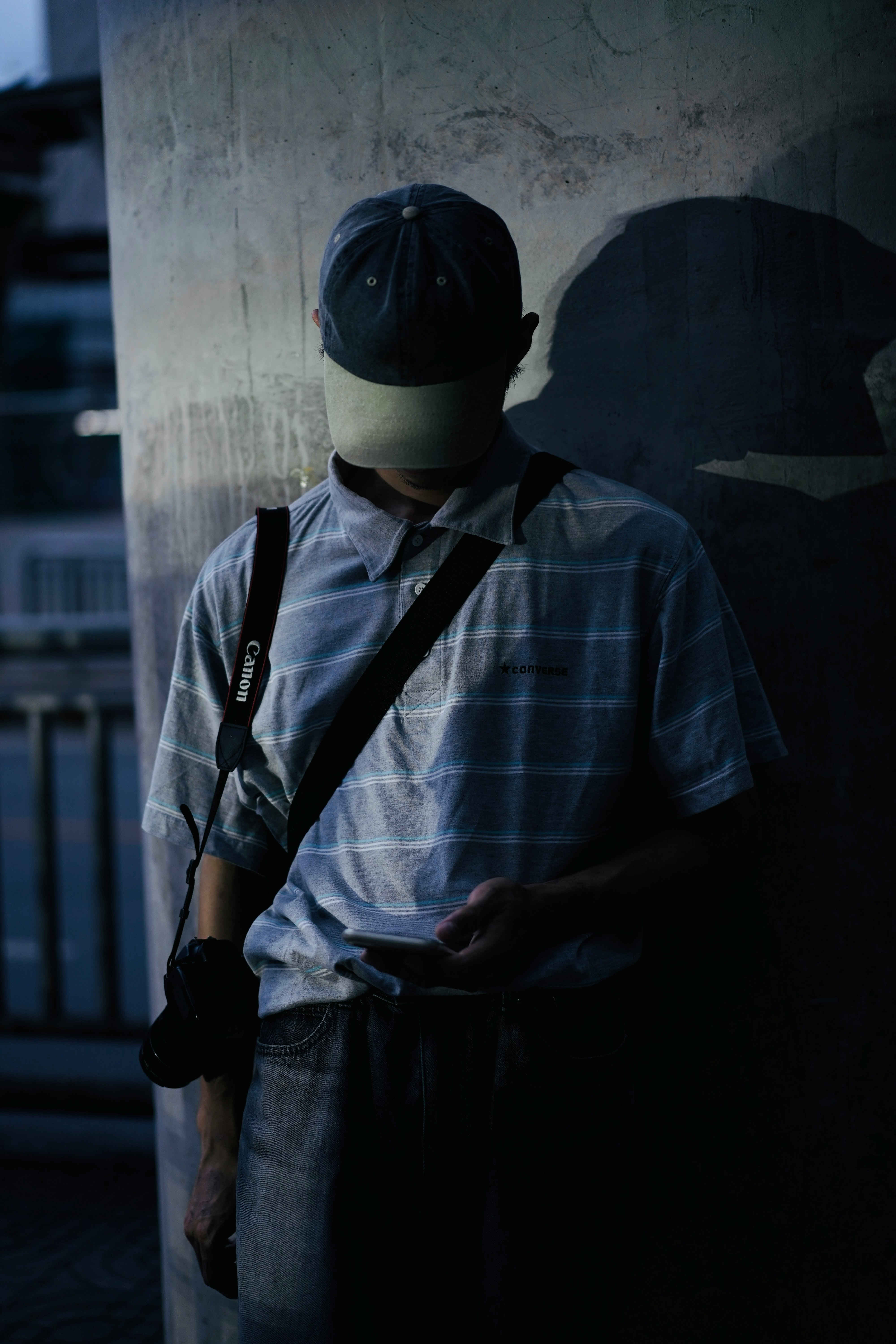 A hat-wearing person holding a camera near a wall