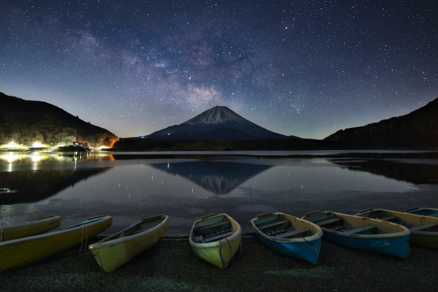 Malersicher Blick auf den Fuji, der sich in einem See unter einem Sternenhimmel mit aufgereihten Kanus spiegelt