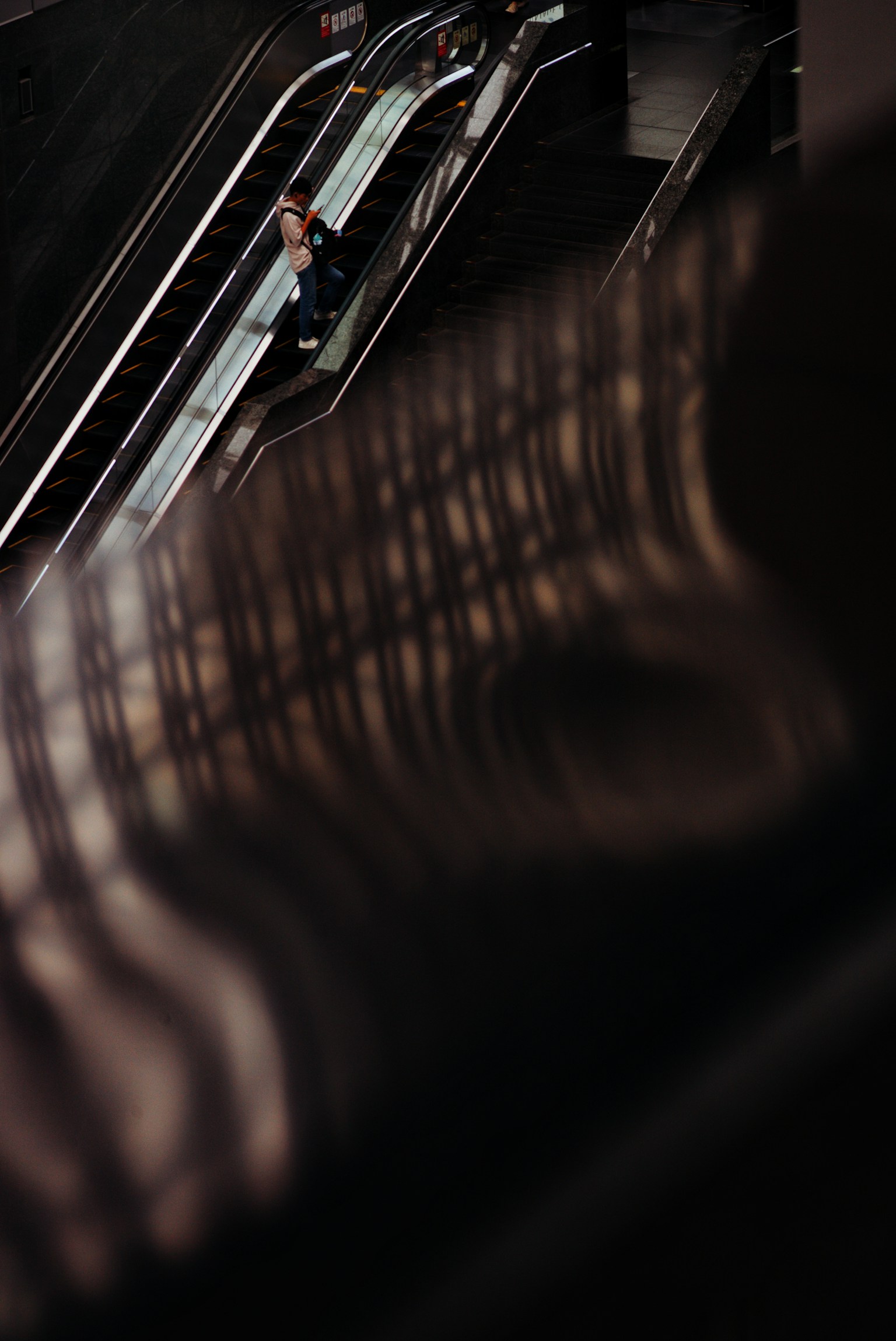 エスカレーターの上に立つ人とその影が映るシーン