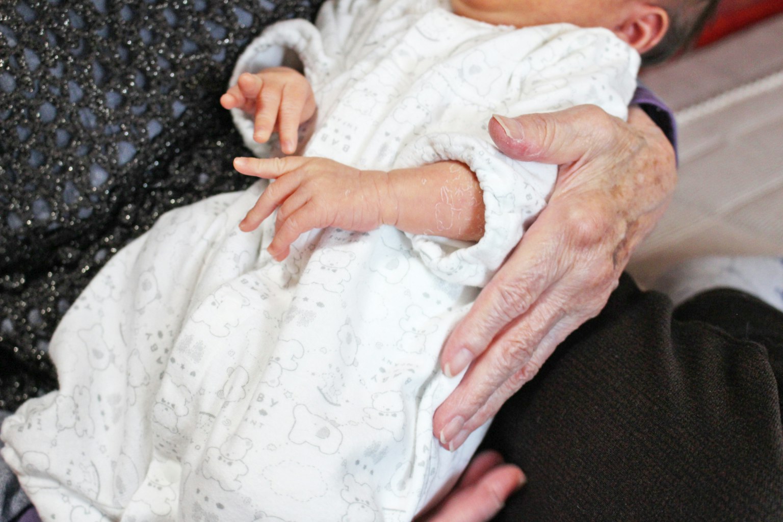 Nahaufnahme eines Babys in einem weißen Outfit, das von einer Hand eines Erwachsenen gehalten wird