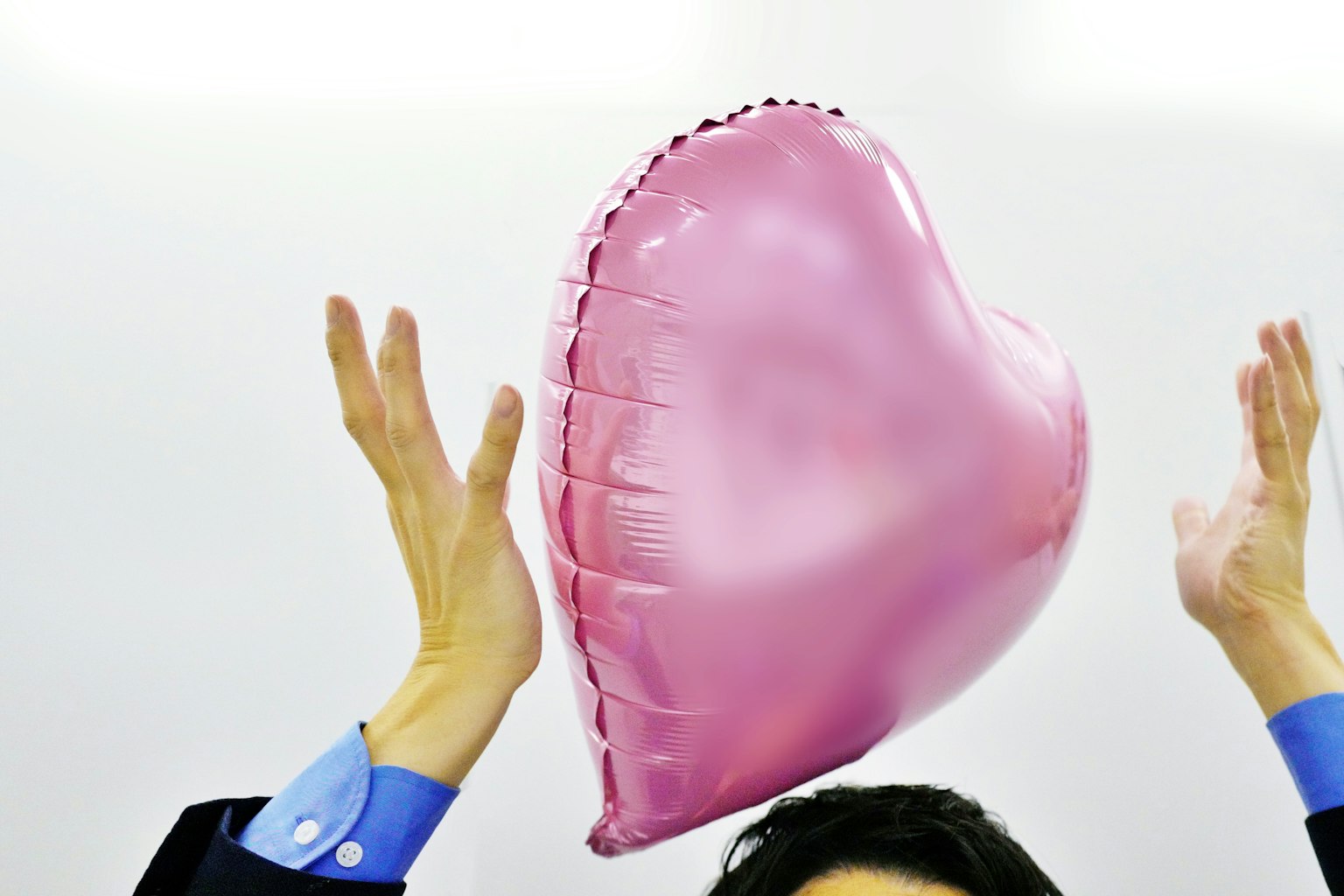 Seorang pria memegang balon berbentuk hati berwarna pink dengan tangan terangkat