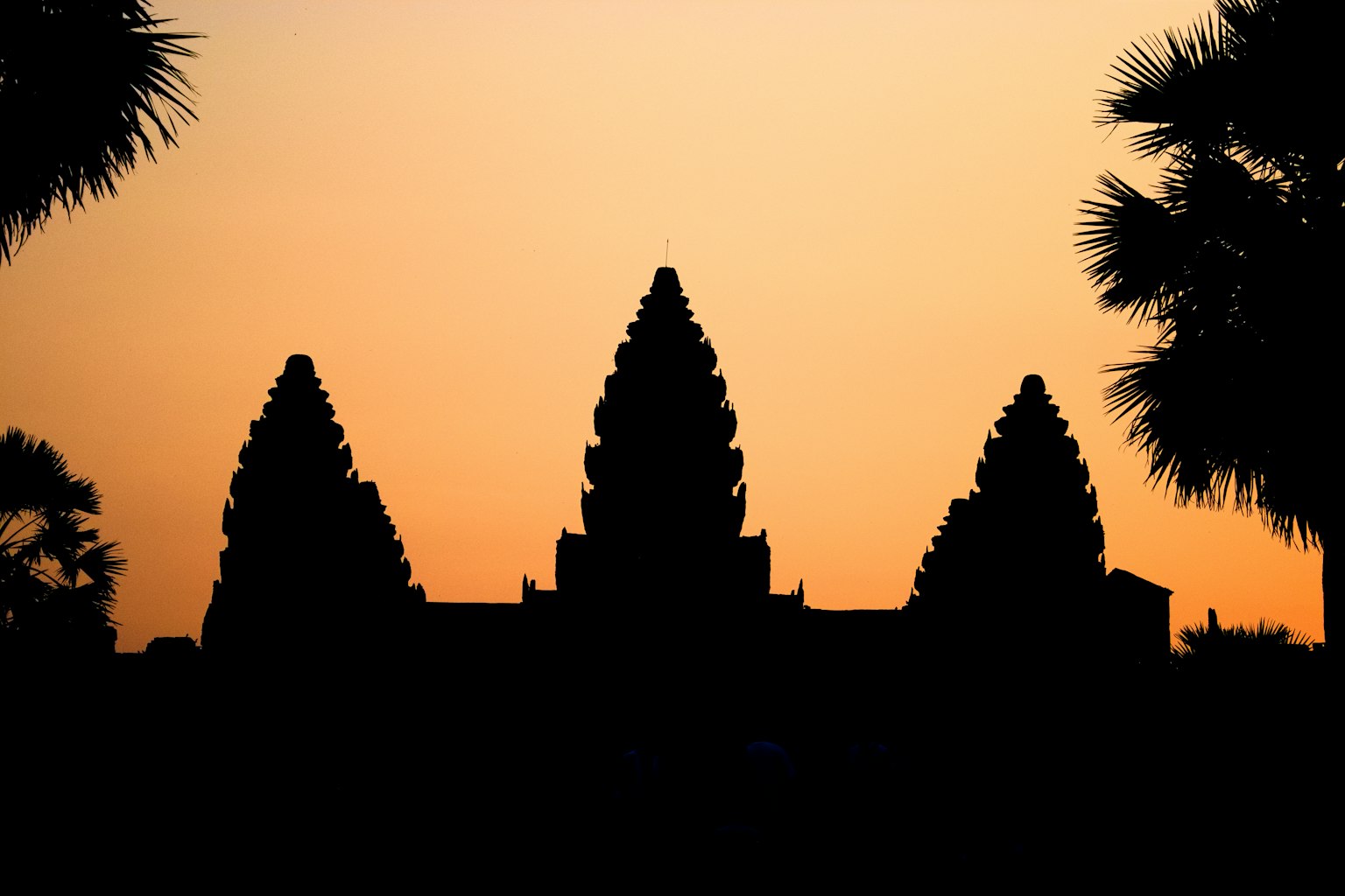 Silhouette di Angkor Wat contro un cielo al tramonto con palme
