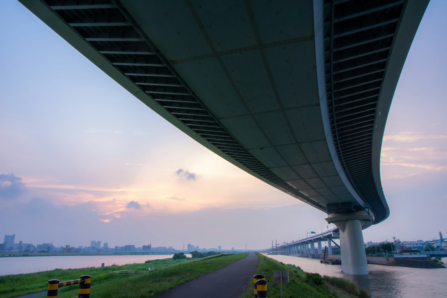View from beneath a curved bridge showing the sunset sky and river