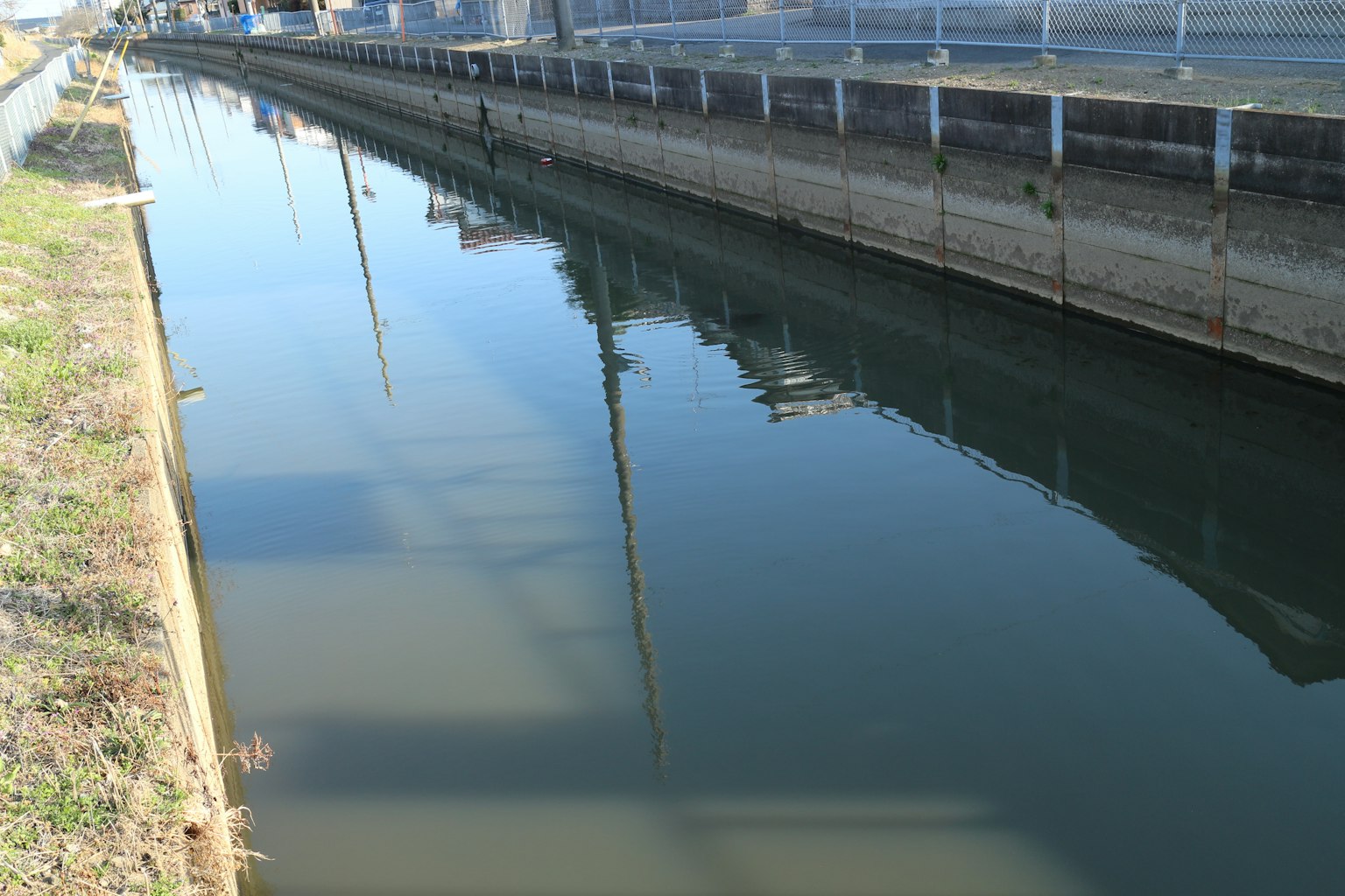 Calm waterway reflecting surrounding buildings and poles