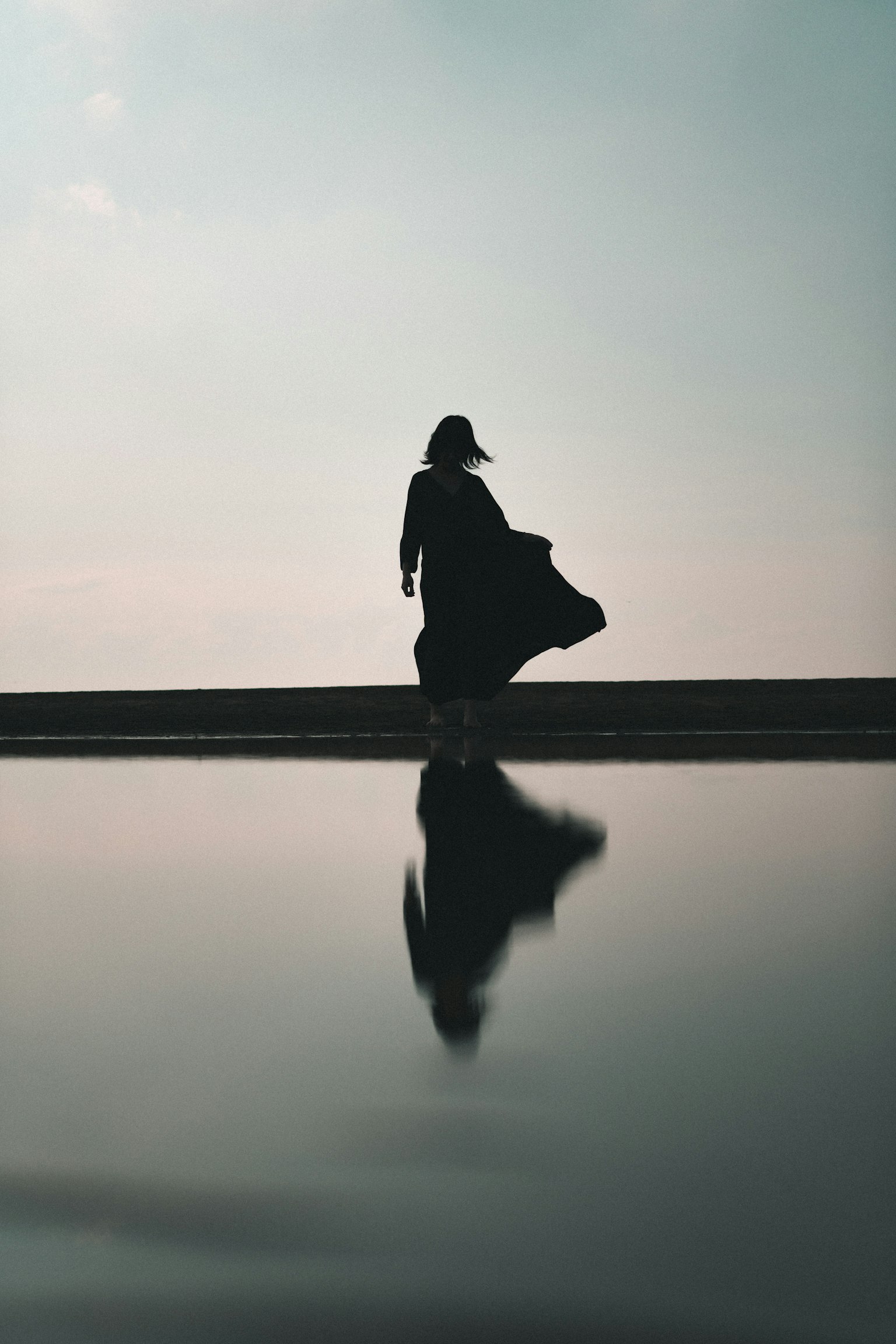 A silhouette of a woman standing against a calm water surface