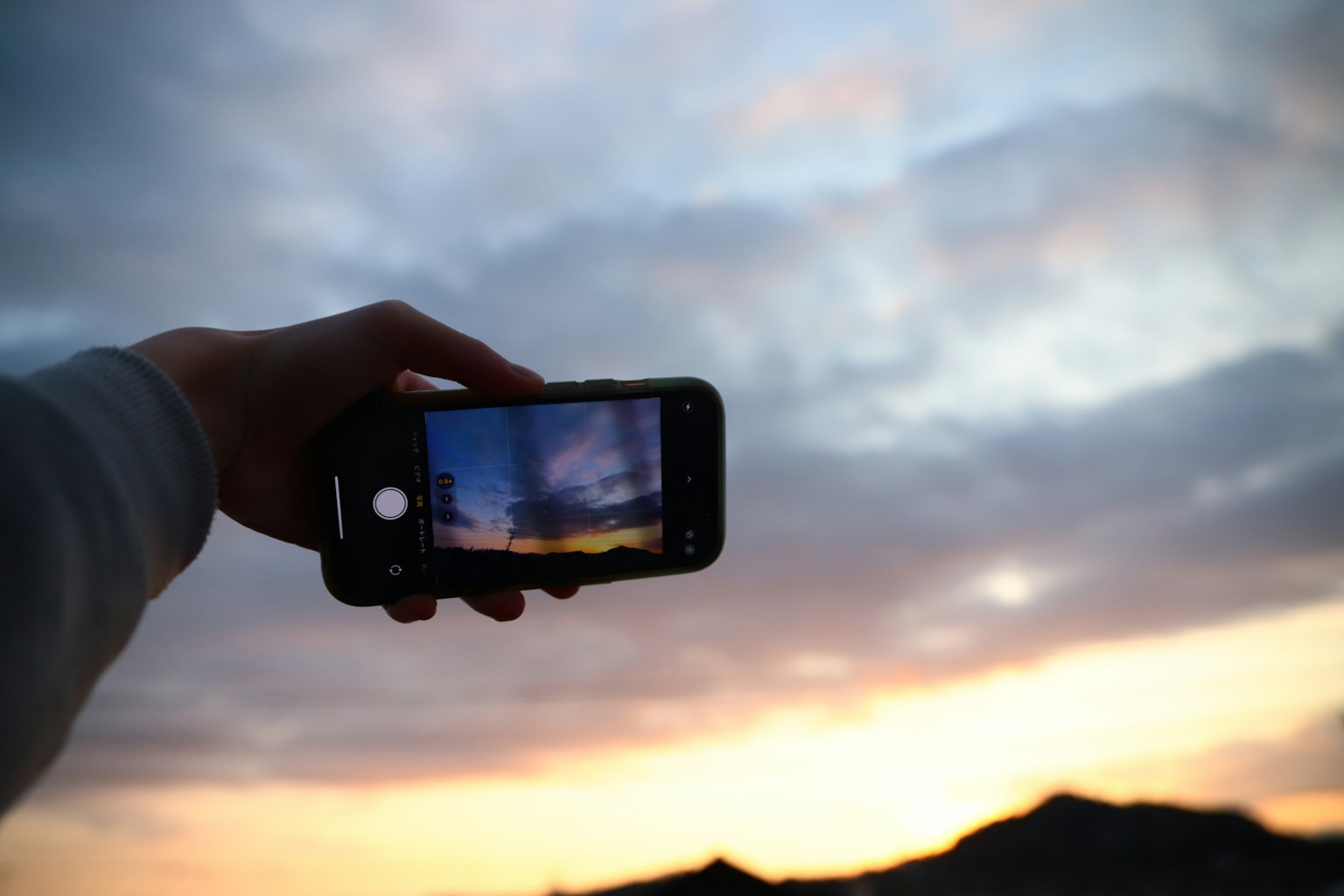 Mano sosteniendo un smartphone capturando un atardecer
