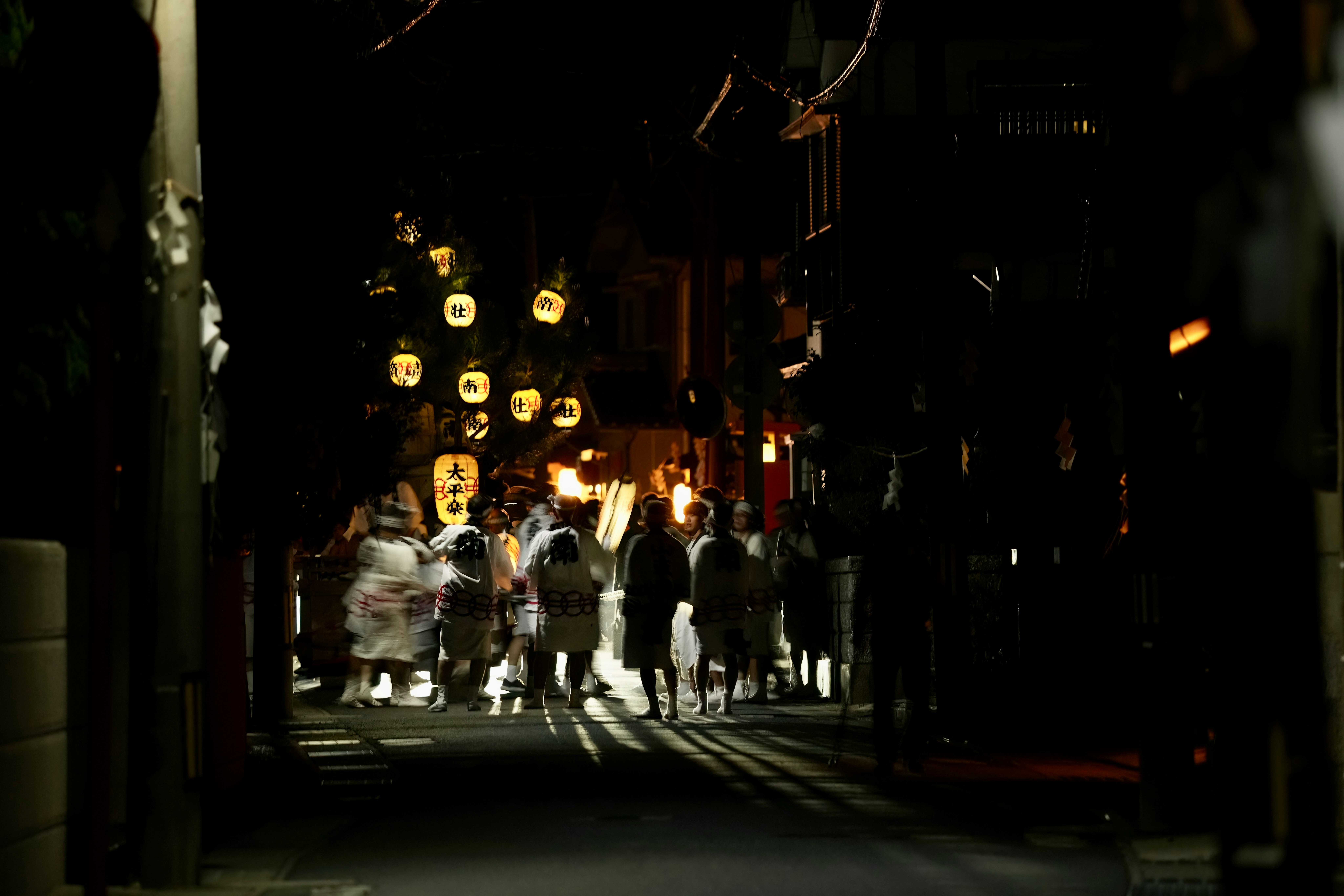 提灯の灯る夜の路地を歩く人々の行列