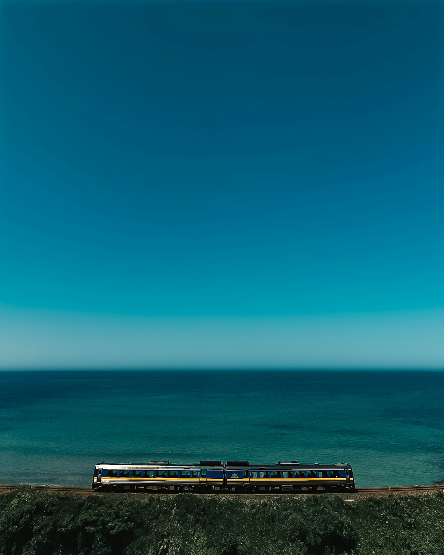 Treno che corre vicino all'oceano sotto un cielo blu chiaro