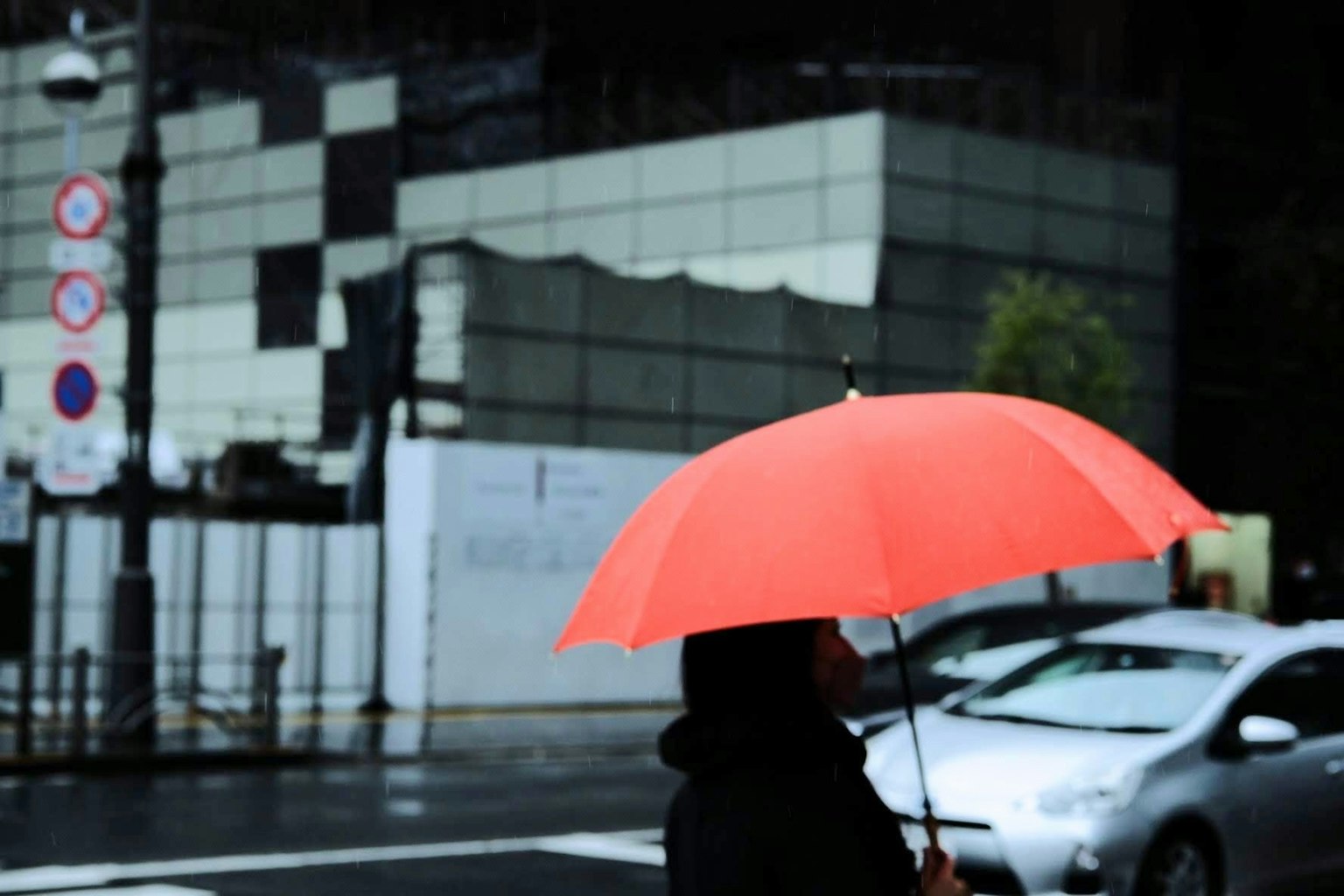 Eine Person mit einem roten Regenschirm steht vor einer urbanen Kulisse
