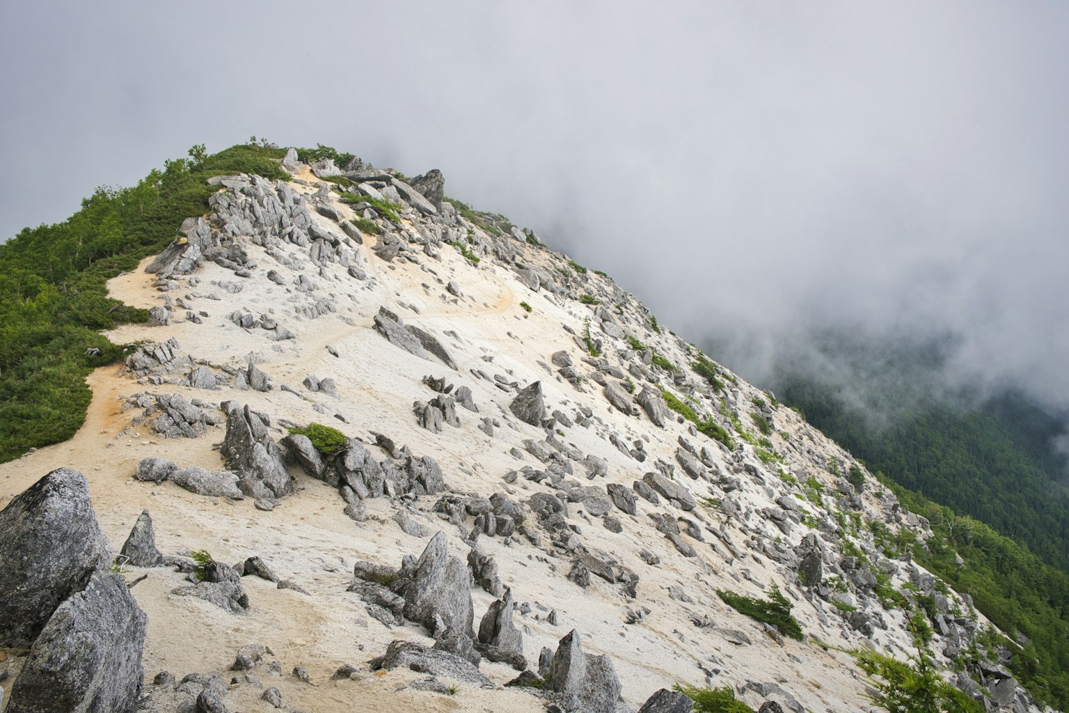 Un versant montagneux rocheux avec de la verdure et des nuages