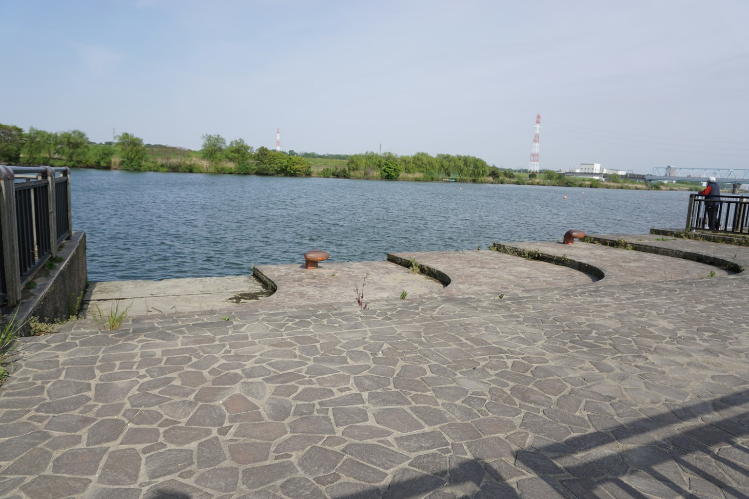 Área pavimentada de piedra junto a un río tranquilo con árboles verdes
