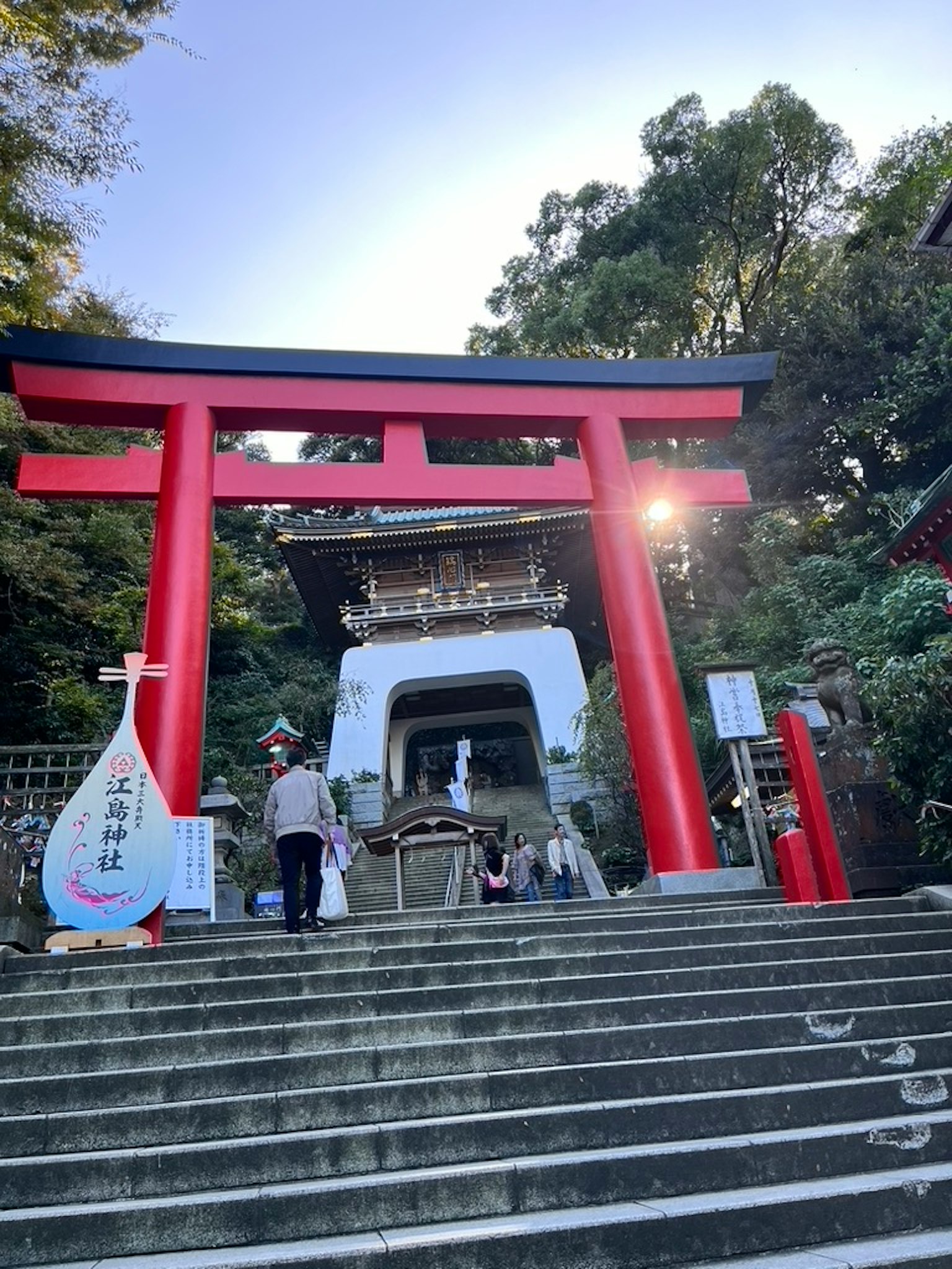 Portale torii rosso e scale del santuario con visitatori e sfondo naturale sereno