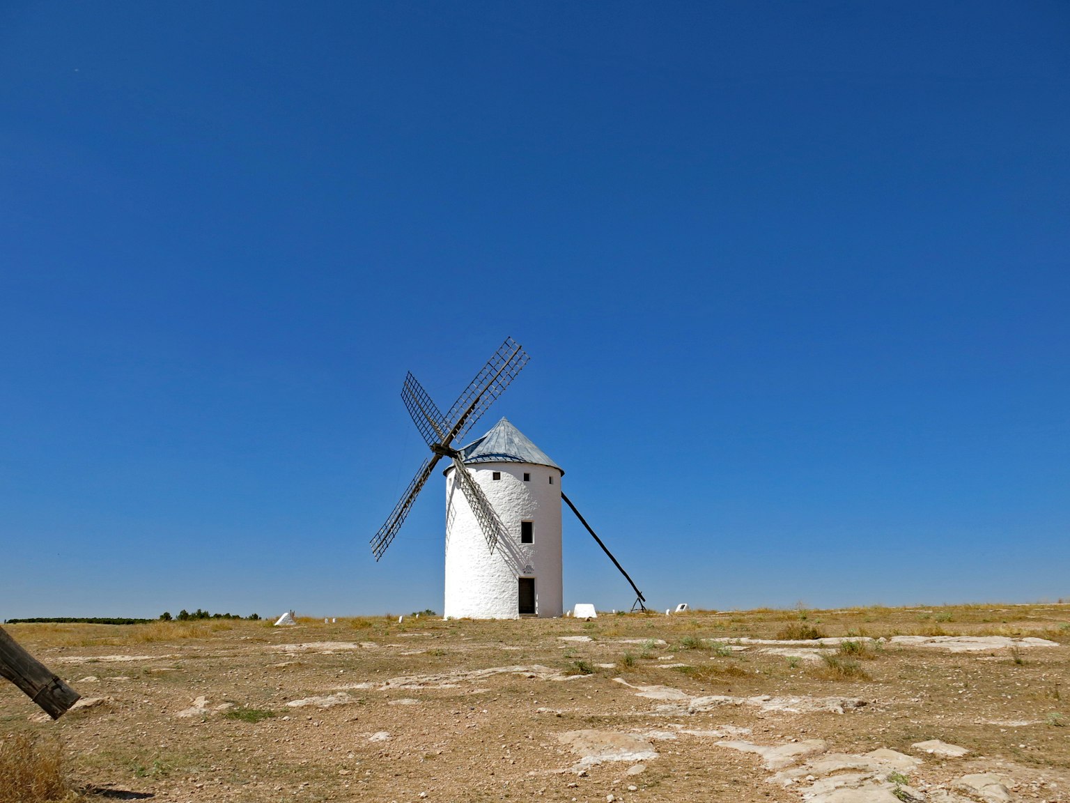 Un molino de viento blanco de pie en un pastizal seco bajo un cielo azul