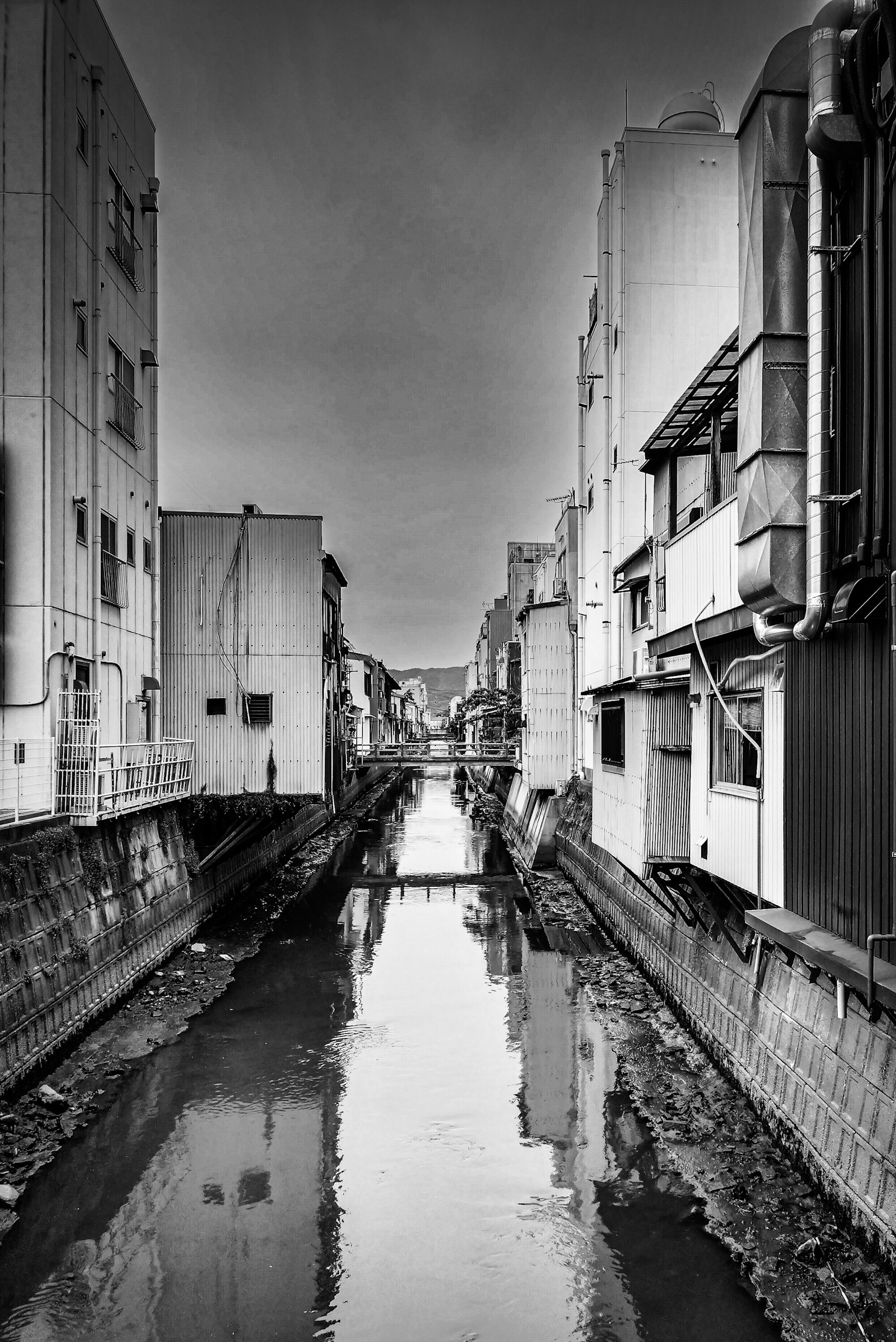 Canal estrecho flanqueado por edificios en una escena urbana en blanco y negro