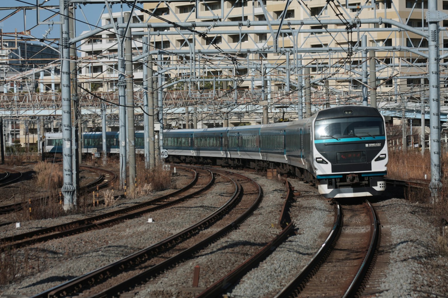 Treno che curva con cavi aerei e edifici vicini