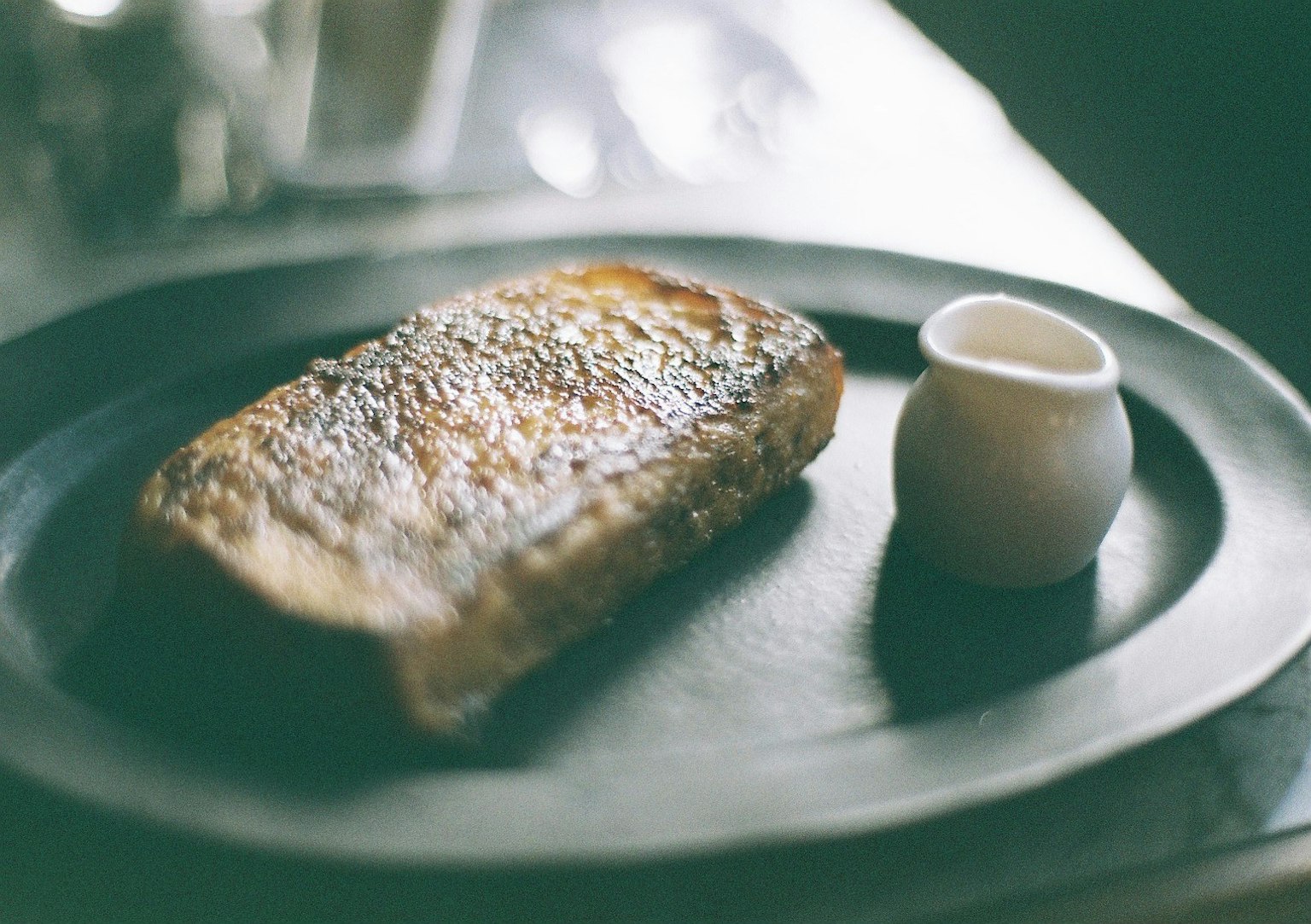 Pain grillé sur une assiette noire avec un petit récipient de sauce blanche