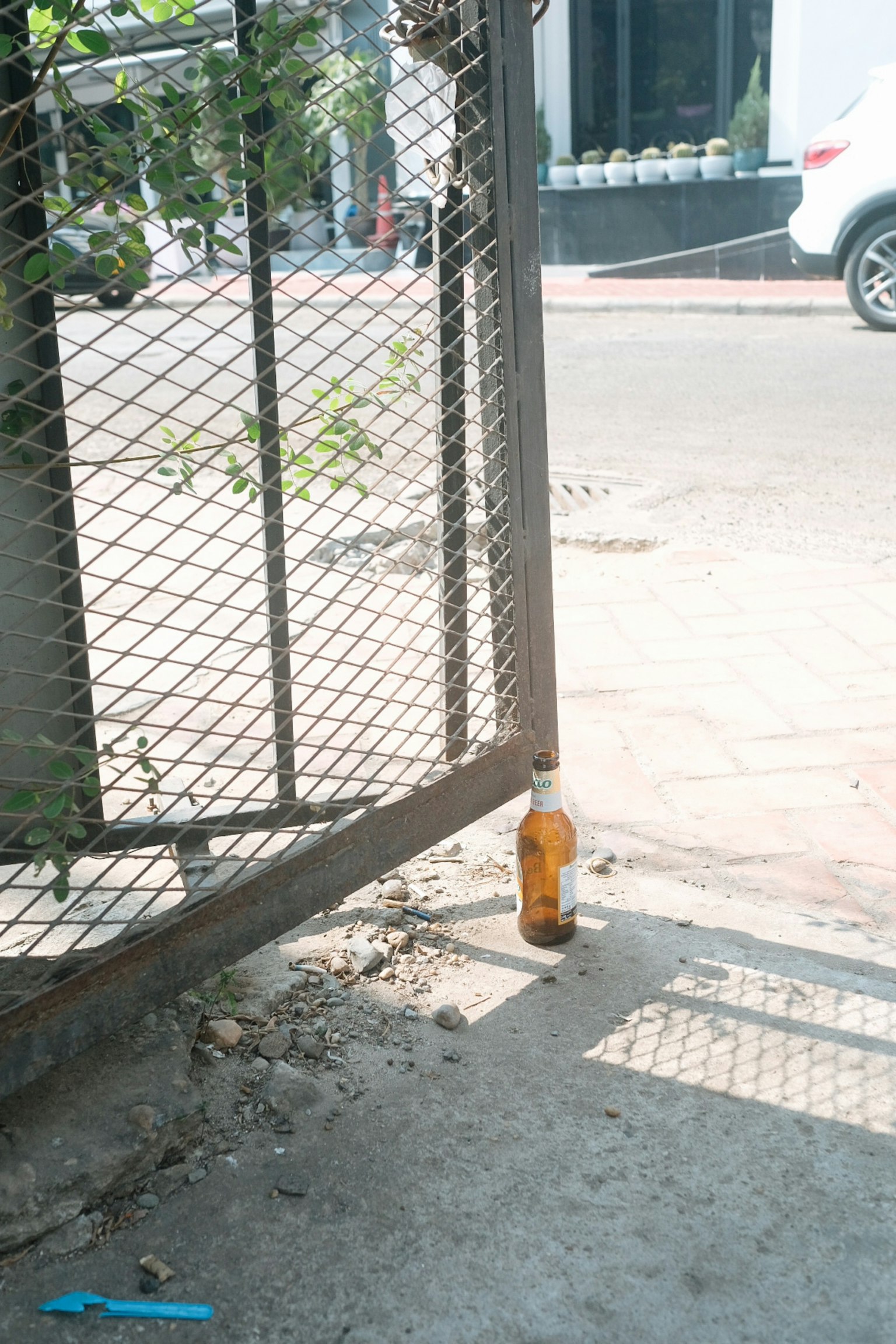 Brown bottle placed at the gap of a gate on a sunlit paved road