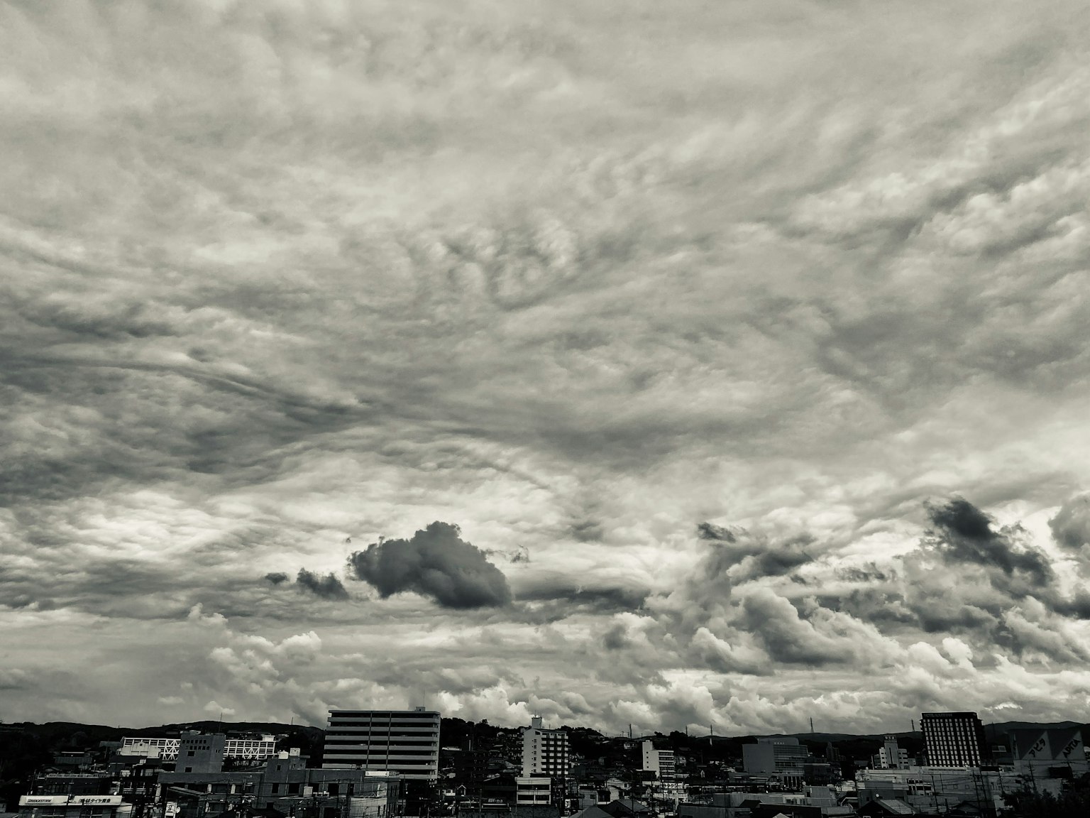 Langit hitam putih dengan awan dramatis dan garis langit kota