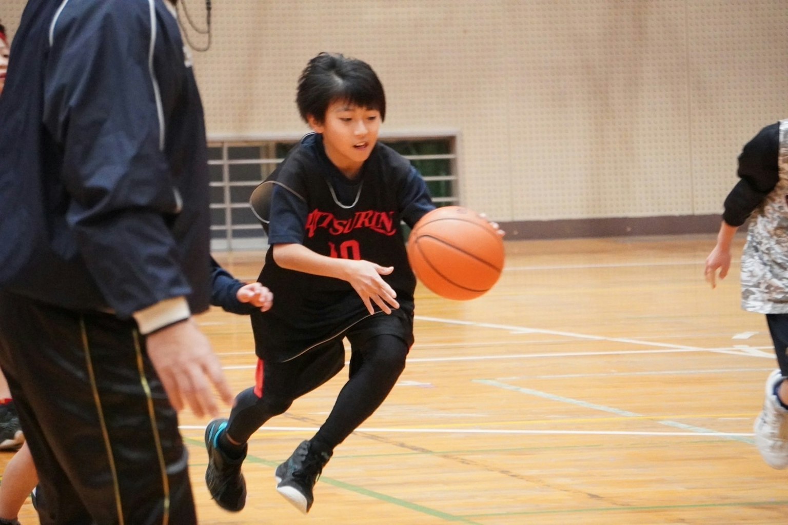 เด็กกำลังวิ่งพร้อมกับลูกบาสเกตบอลในยิมระหว่างการฝึกซ้อมกับโค้ช