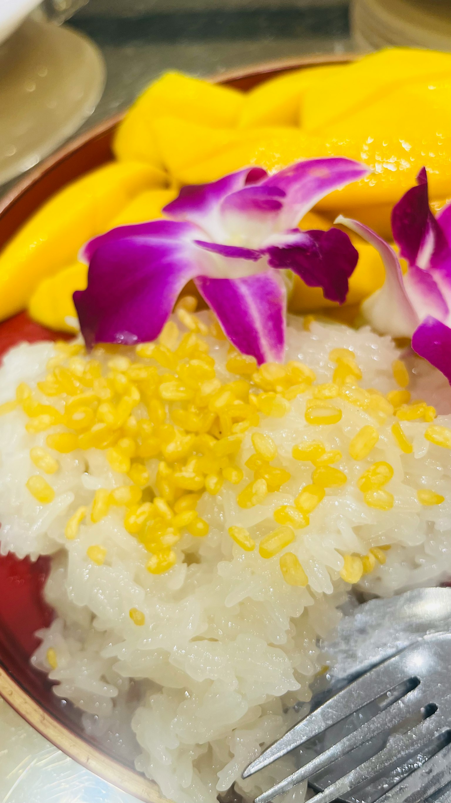 芒果糯米甜点配椰子和黄色绿豆，加上紫色兰花装饰