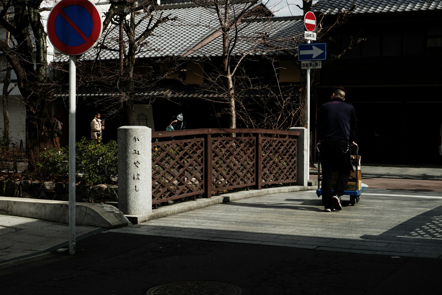 一个人推着手推车穿过街道，背景中有一座老建筑和木栅栏