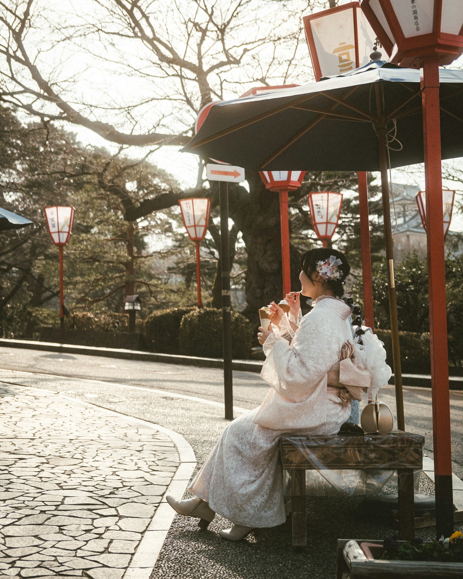 A woman in a kimono sitting on a bench surrounded by lanterns