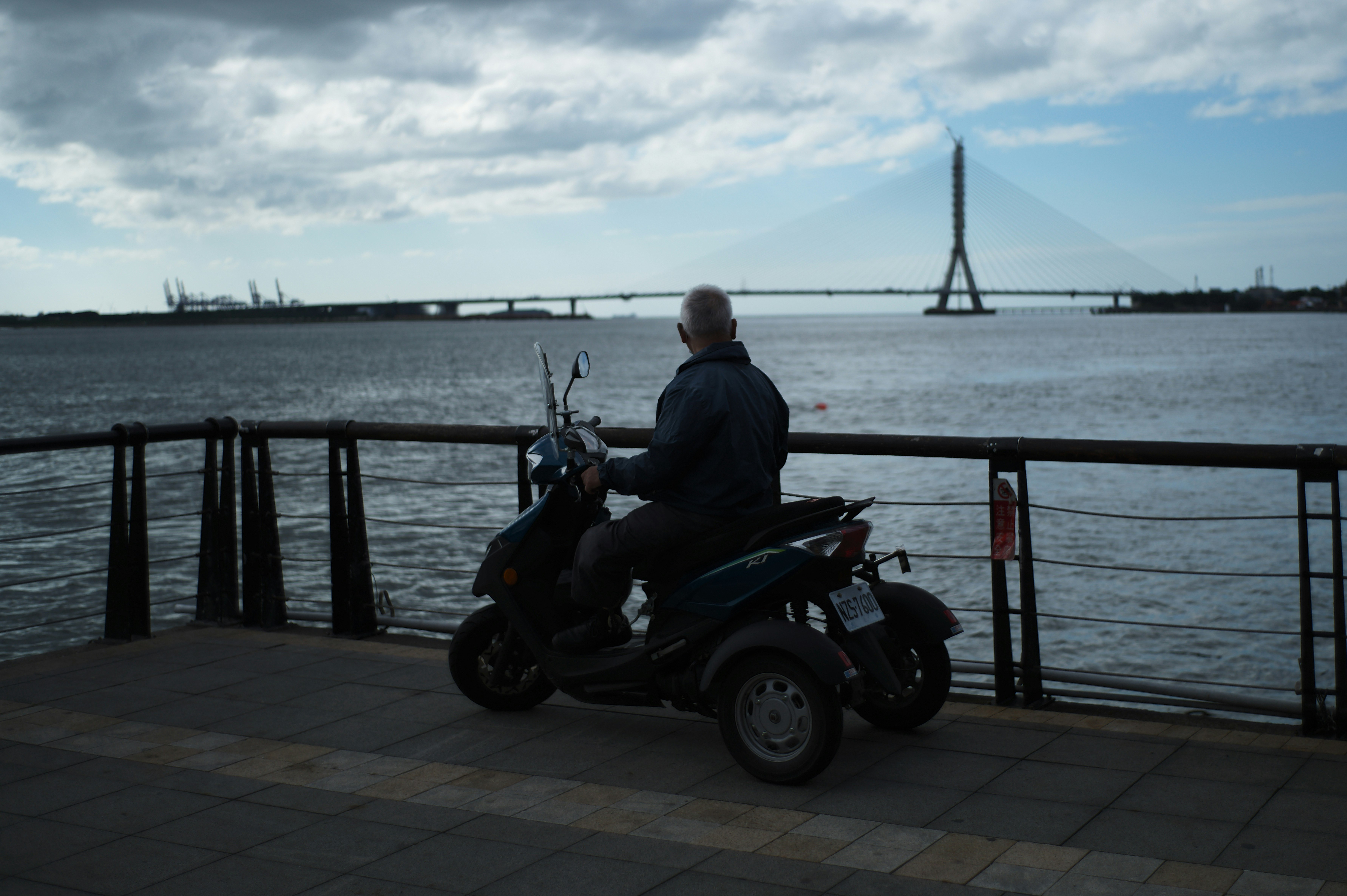 海辺の防波堤でバイクに乗る人物と遠くの塔