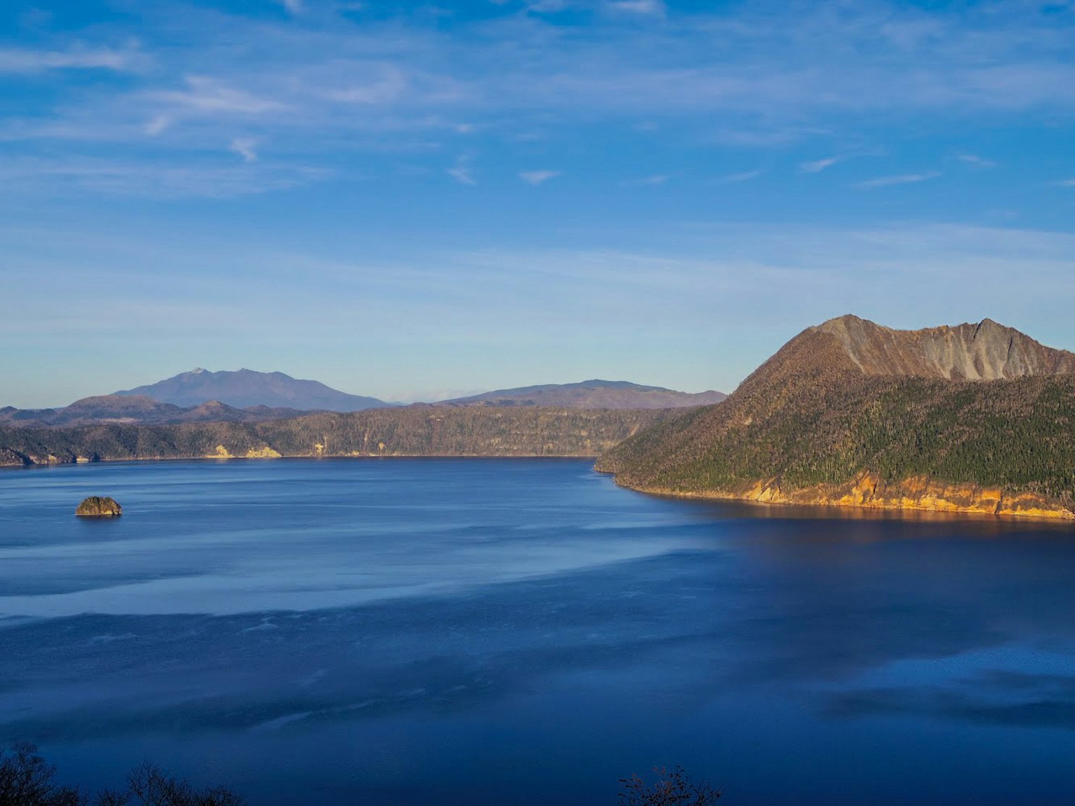 Vue panoramique d'un lac entouré de montagnes sous un ciel bleu clair