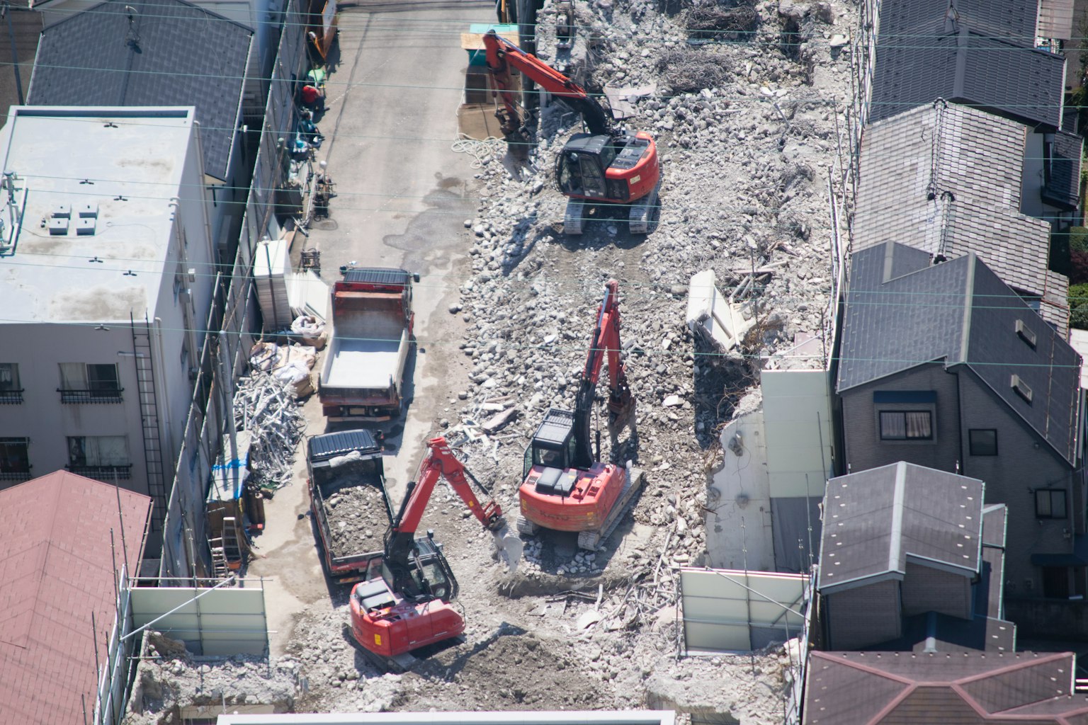 Vista aerea di un cantiere con due escavatori rossi circondati da detriti e edifici danneggiati