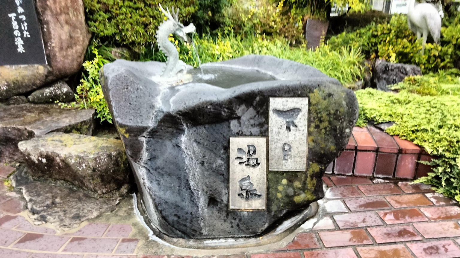Bassin d'eau en pierre avec un jet de dragon et une signalisation en kanji