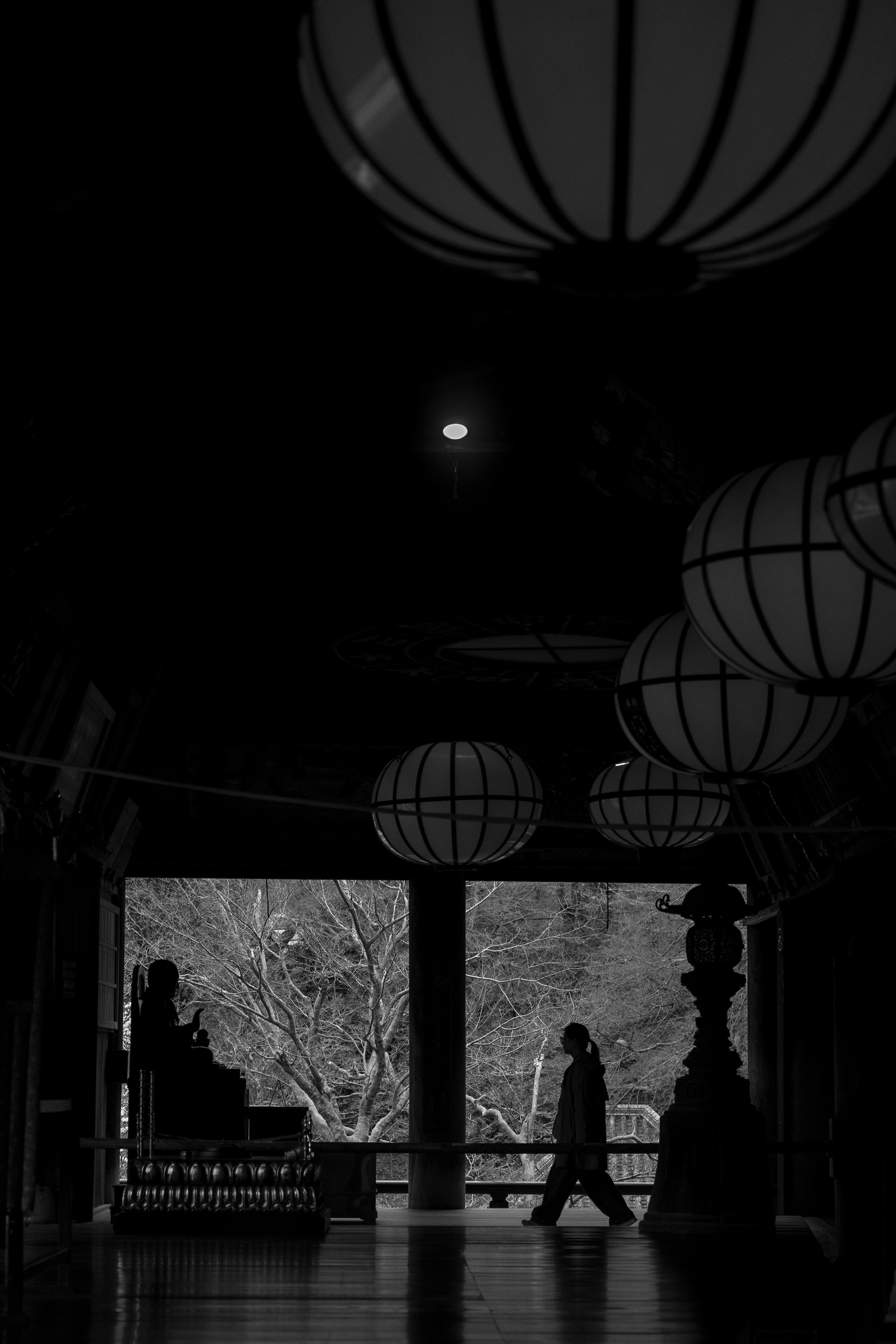 黒い影の中を歩く人物と提灯のある寺院の内部