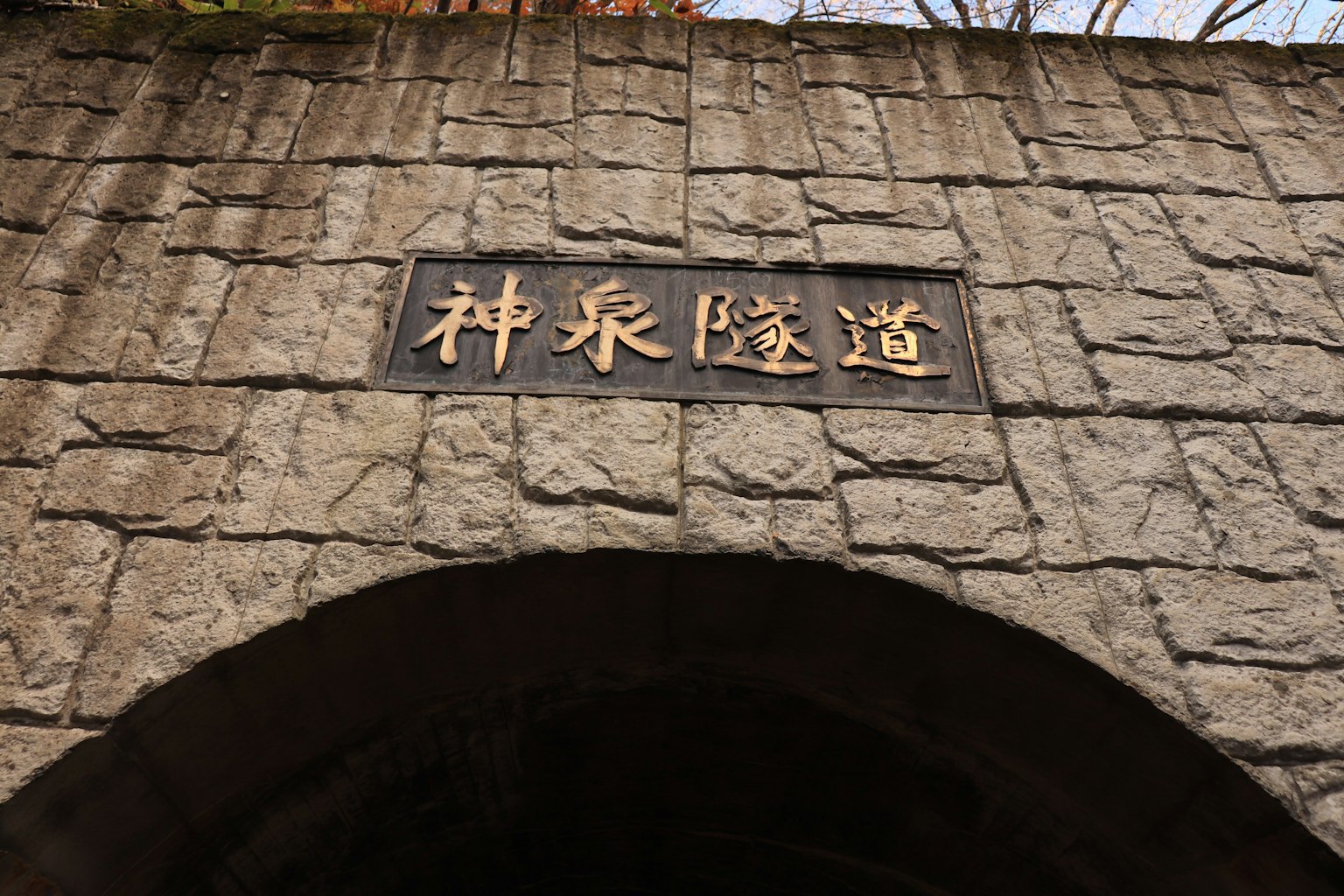 Goldenes Schild mit der Aufschrift Shenquan Tunnel auf einem Steinbogen