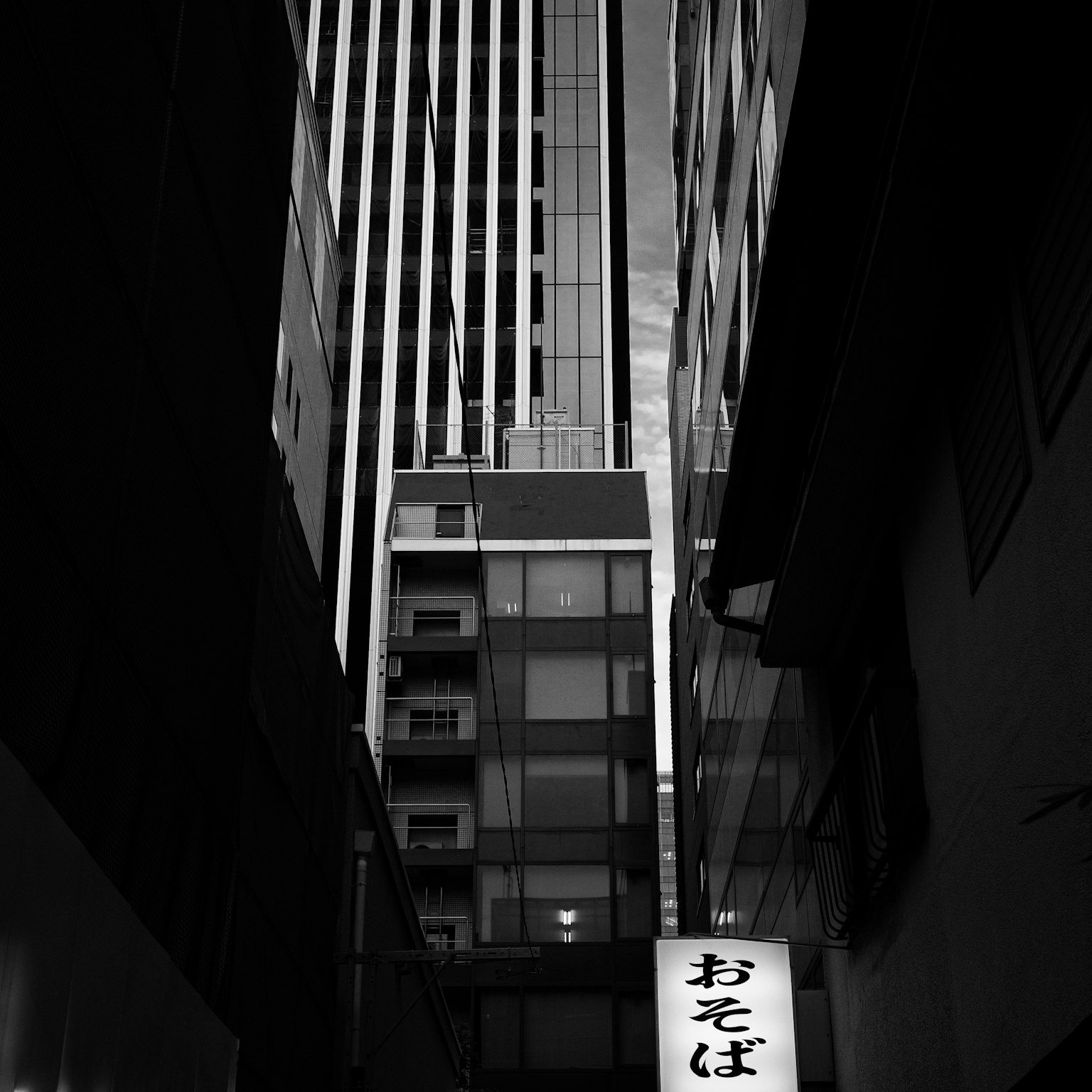 Callejón estrecho con un letrero de soba y edificios altos