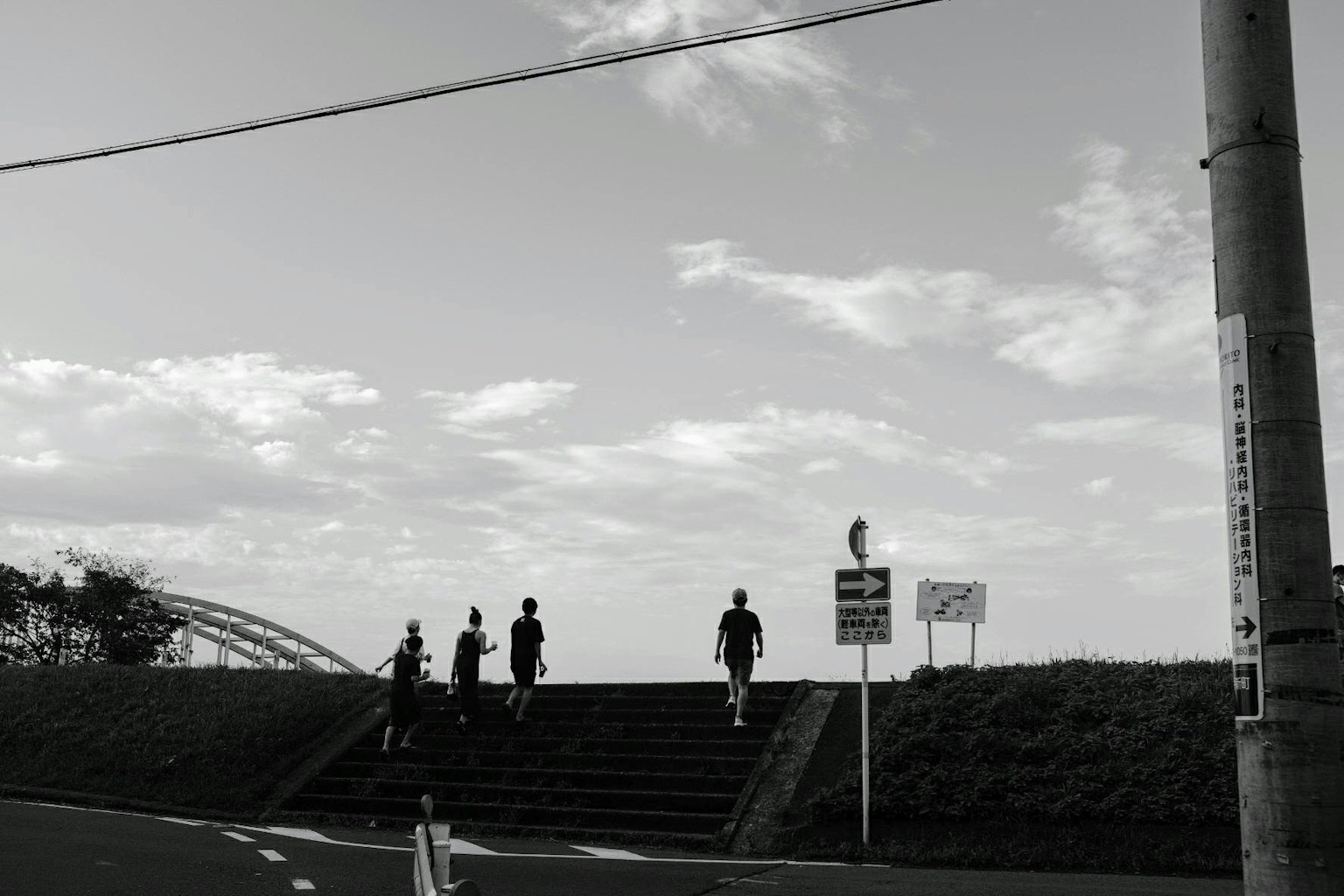 Silhouettes of people ascending stairs against a cloudy sky