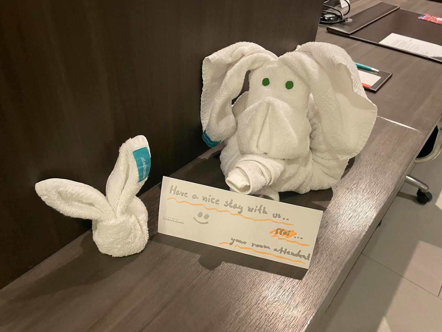 Esculturas de toallas blancas de un conejo pequeño y un conejo grande con ojos verdes sobre una superficie de madera