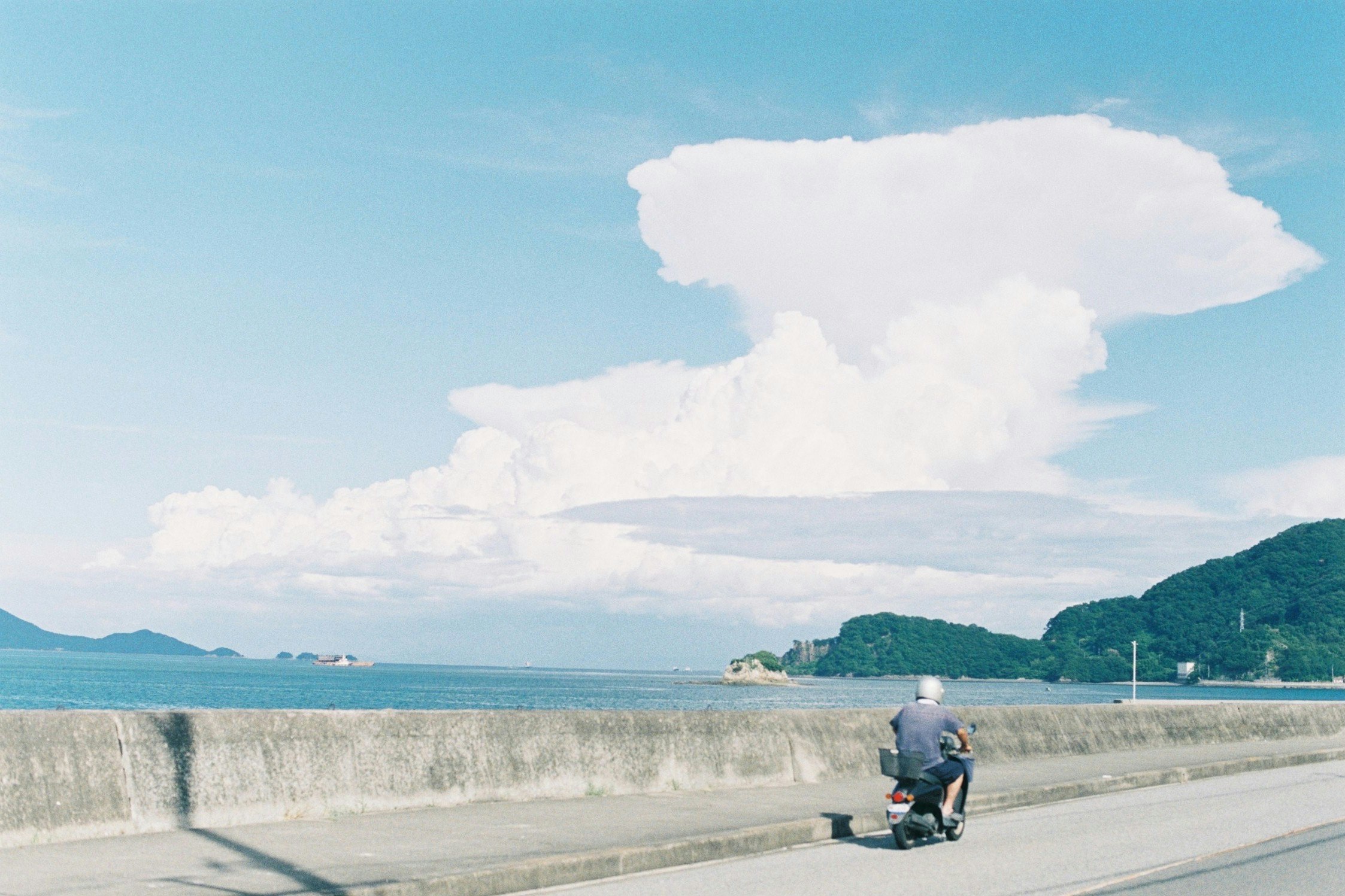 真夏の海辺の防波堤を歩く人と青い空の風景