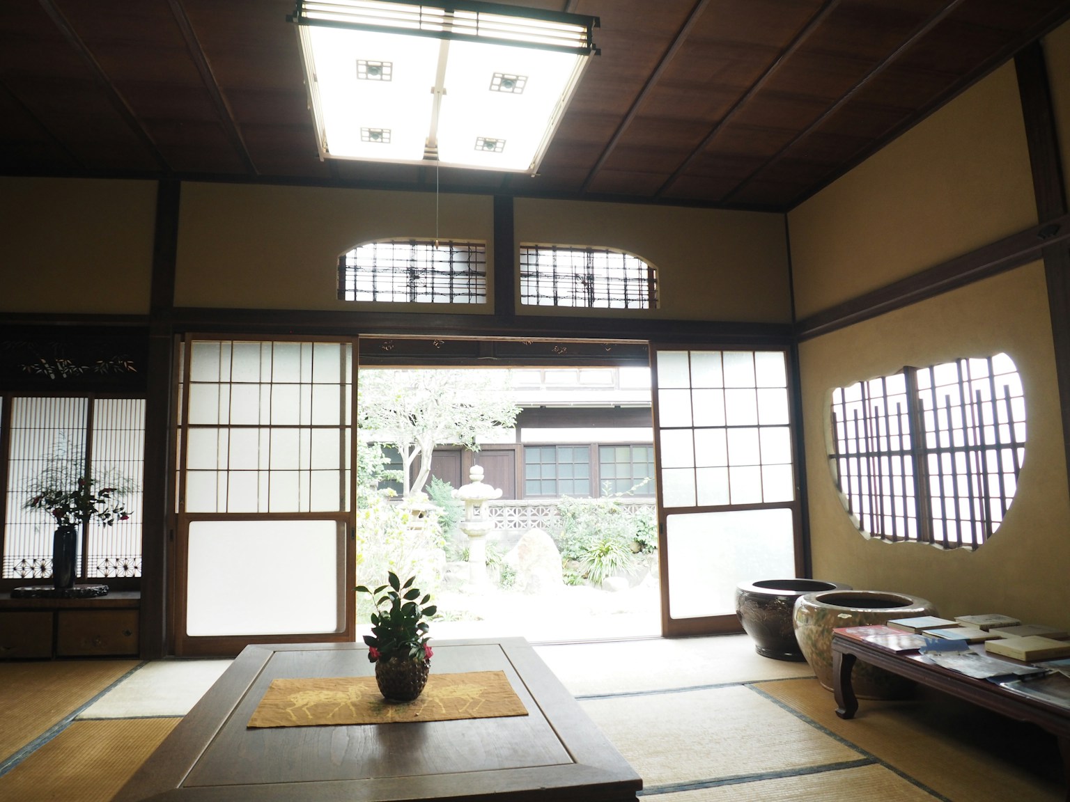 Traditionelles japanisches Interieur mit hellem Licht, Tatami-Boden, Schiebetüren, die einen Garten zeigen, einfacher Tisch mit einer Pflanze