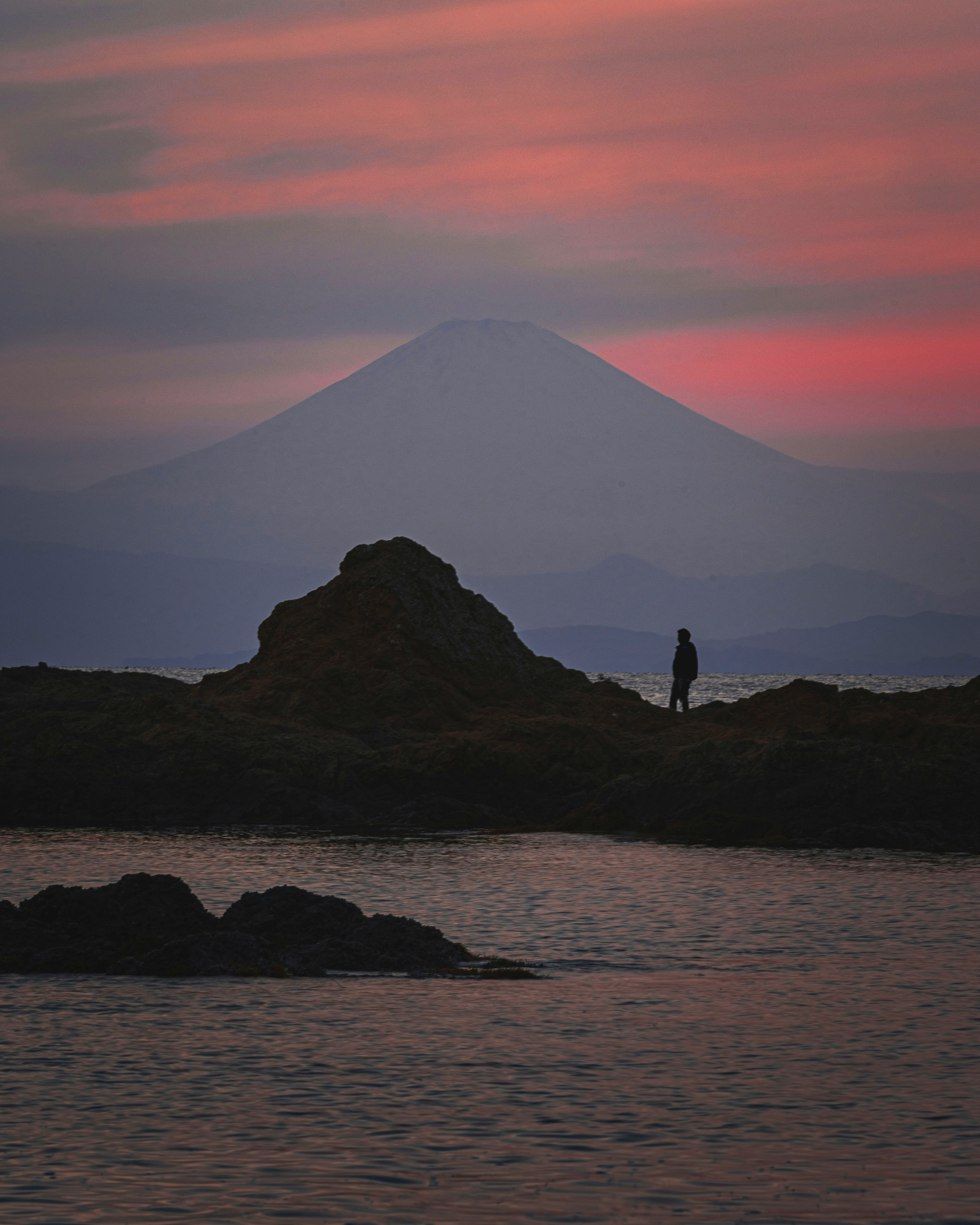 夕焼けの海辺にそびえる火山と人影