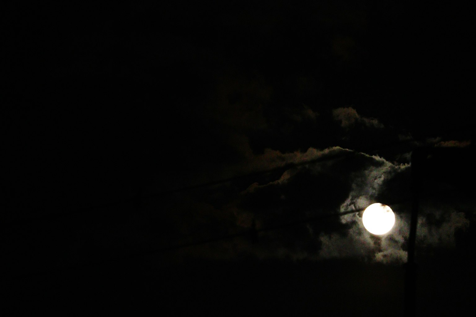 Luna llena brillante en un cielo oscuro con siluetas de nubes