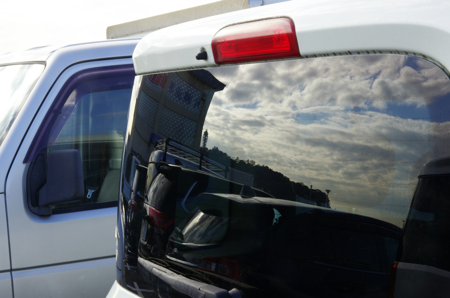Reflexion von Wolken auf der Heckscheibe eines weißen Fahrzeugs neben einem anderen Auto