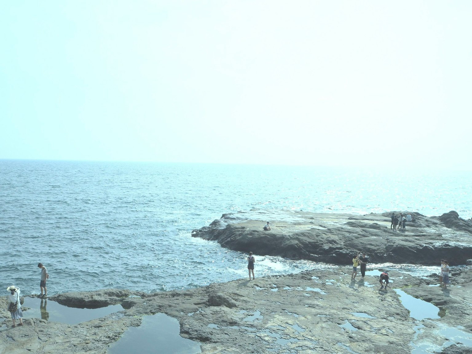 People standing on rocky shore with beautiful ocean view